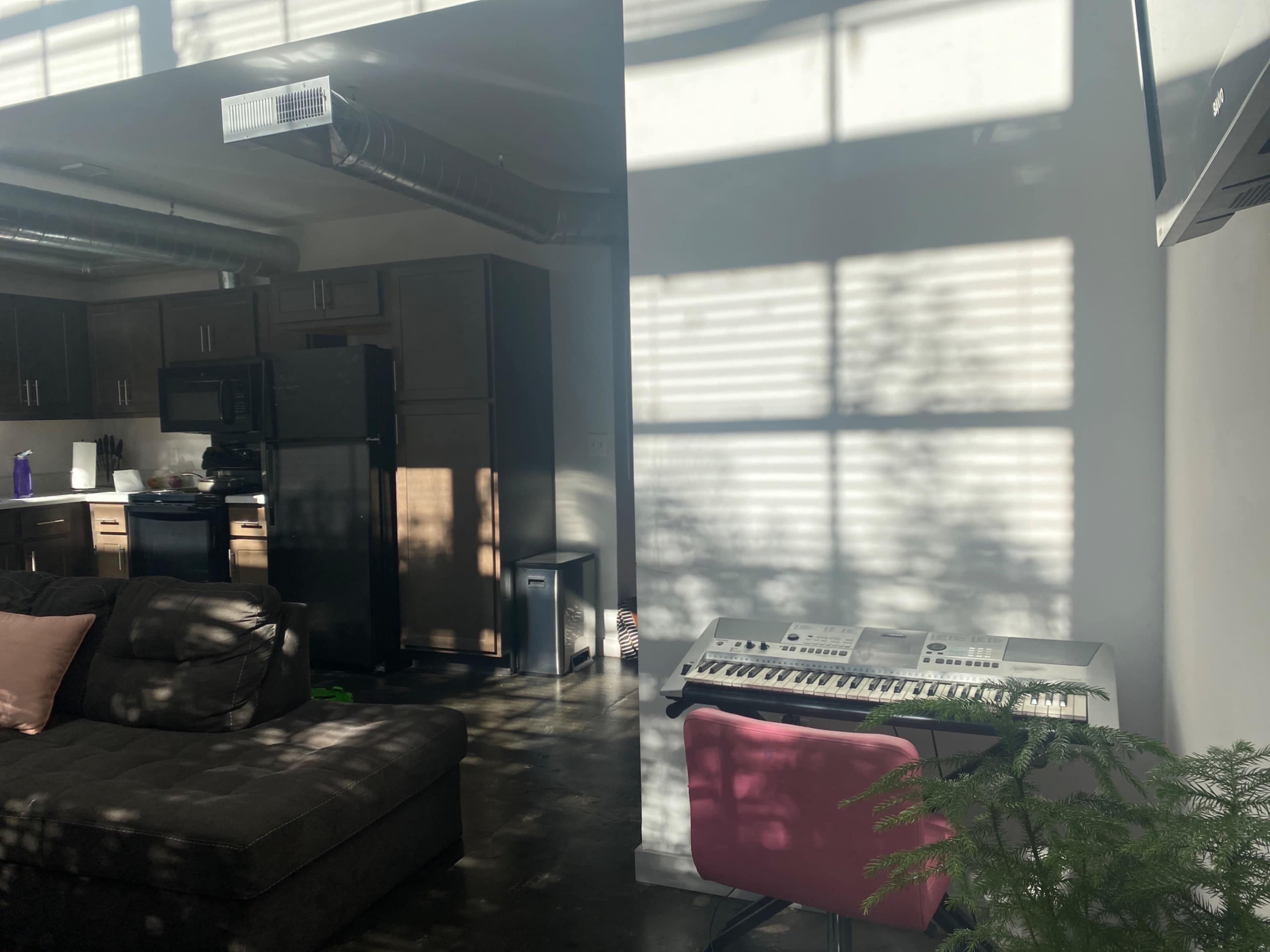 A keyboard sits next to a sofa in a living area illuminated by sunlight filtering through window blinds.