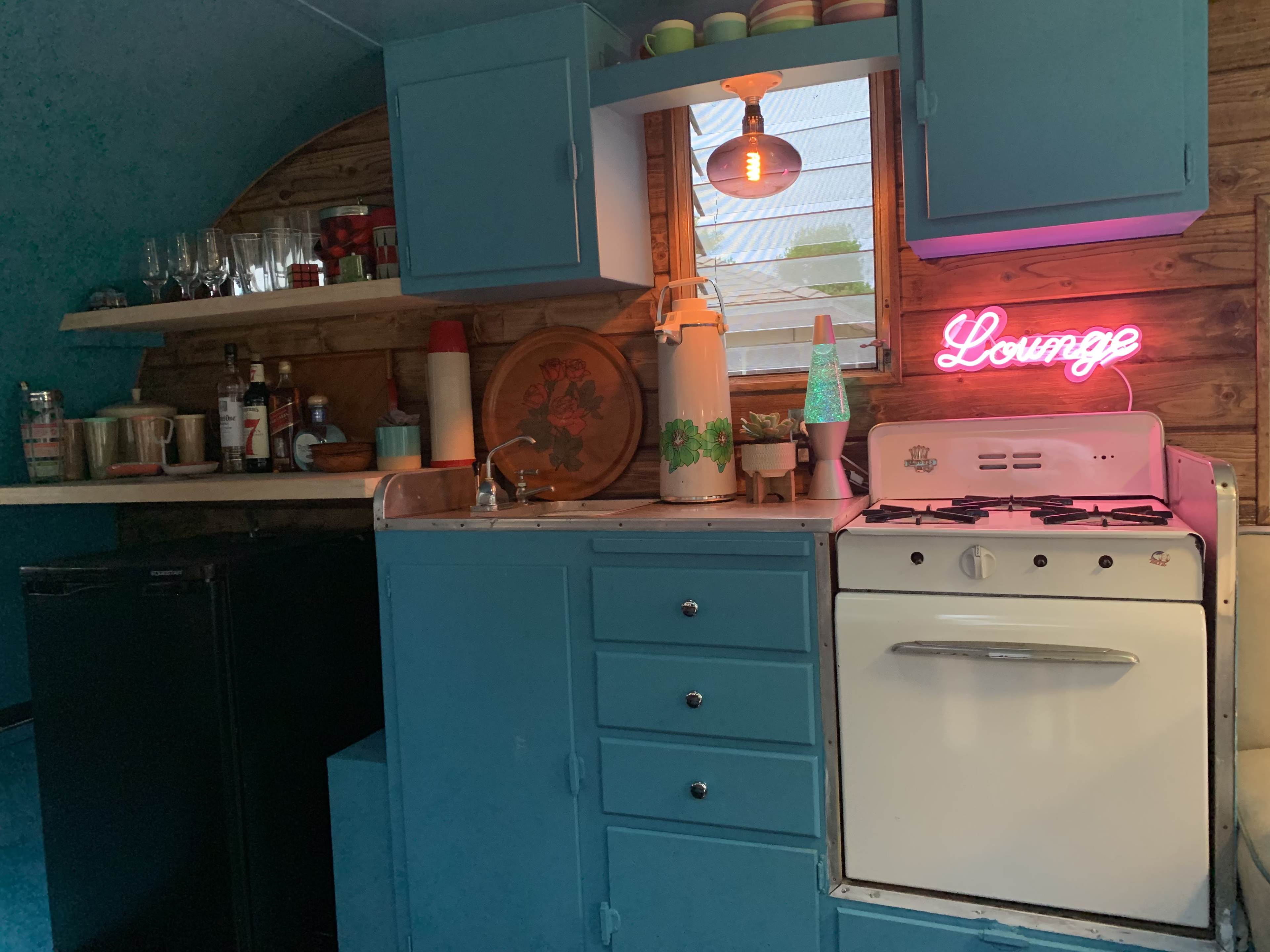 A vintage-style kitchen with teal cabinets, a white stove, and a neon sign that reads "Lounge."