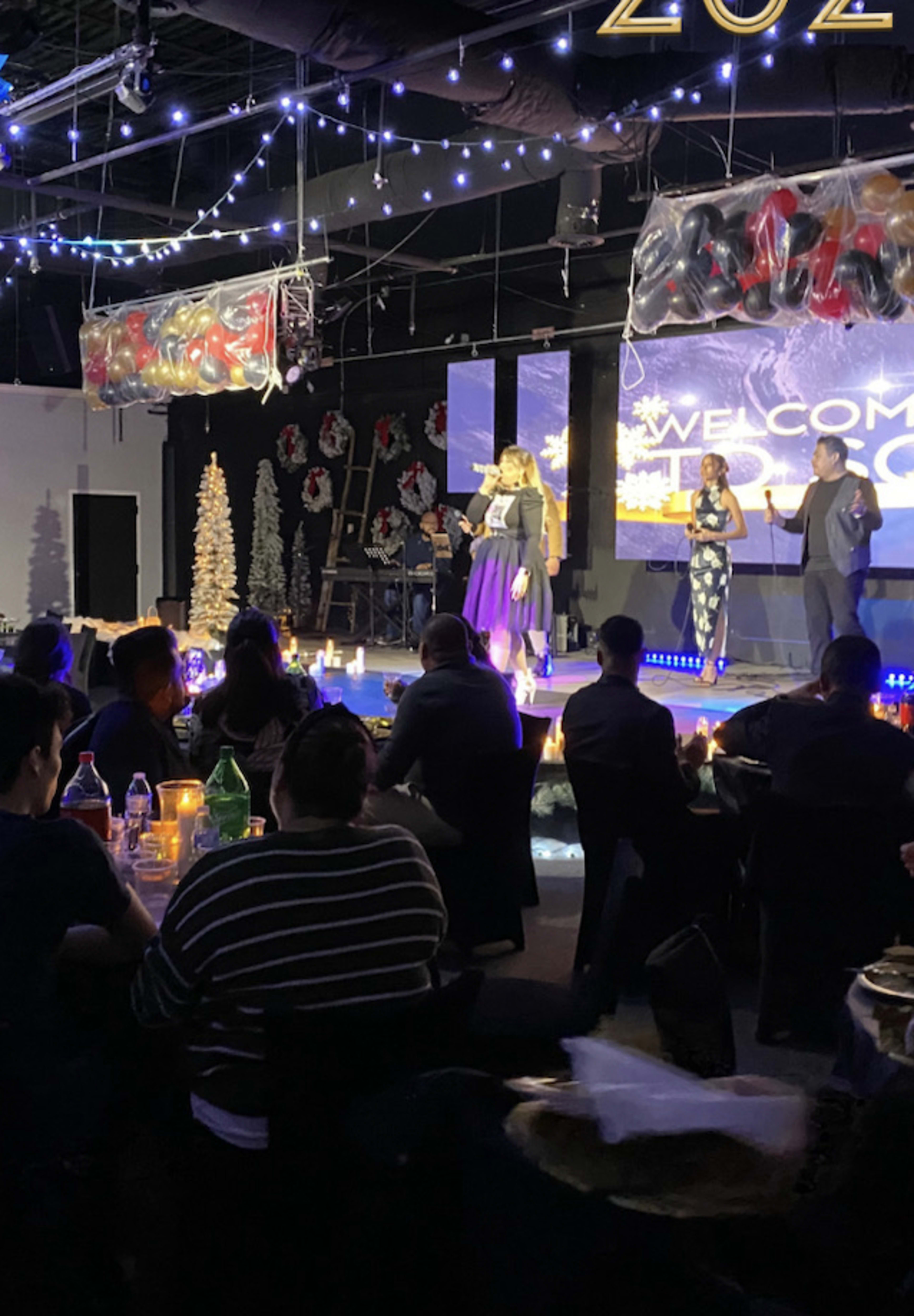 A stage is set up for a New Year's event, featuring a speaker, decorations, and tables filled with guests.