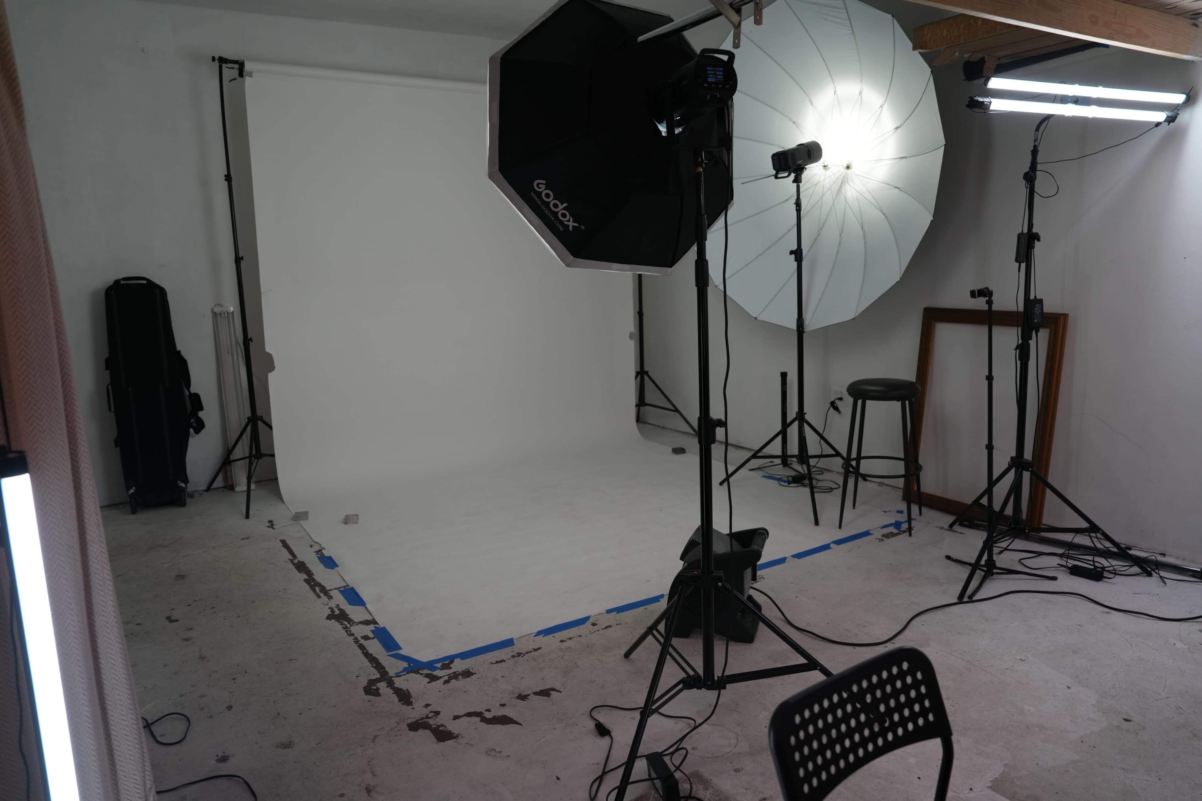 A photography studio setup with a blank white backdrop, lighting equipment, and a few stools and stands.