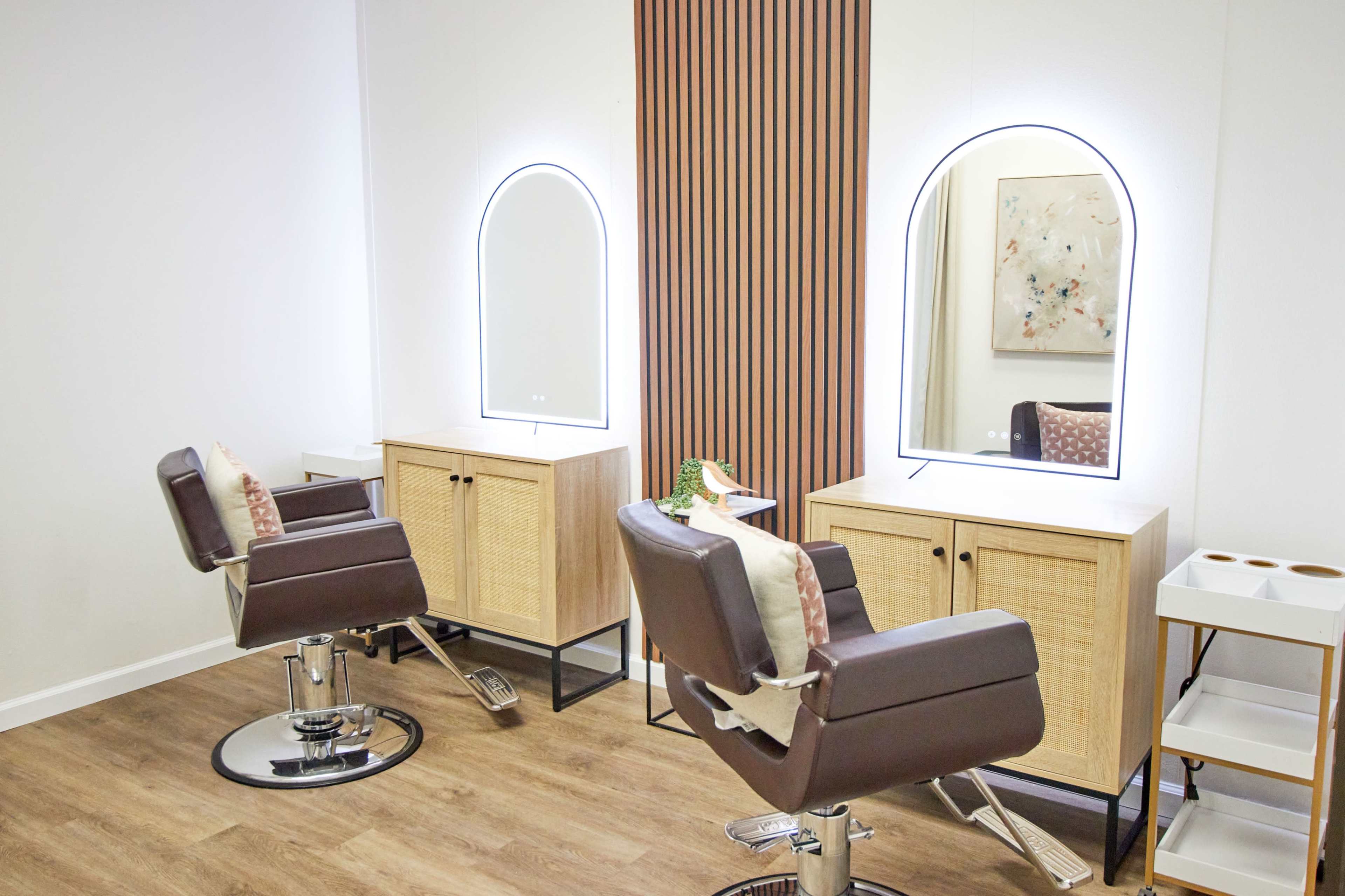 A modern hair salon with two mirrored stations, each featuring a styling chair and wooden storage cabinets.