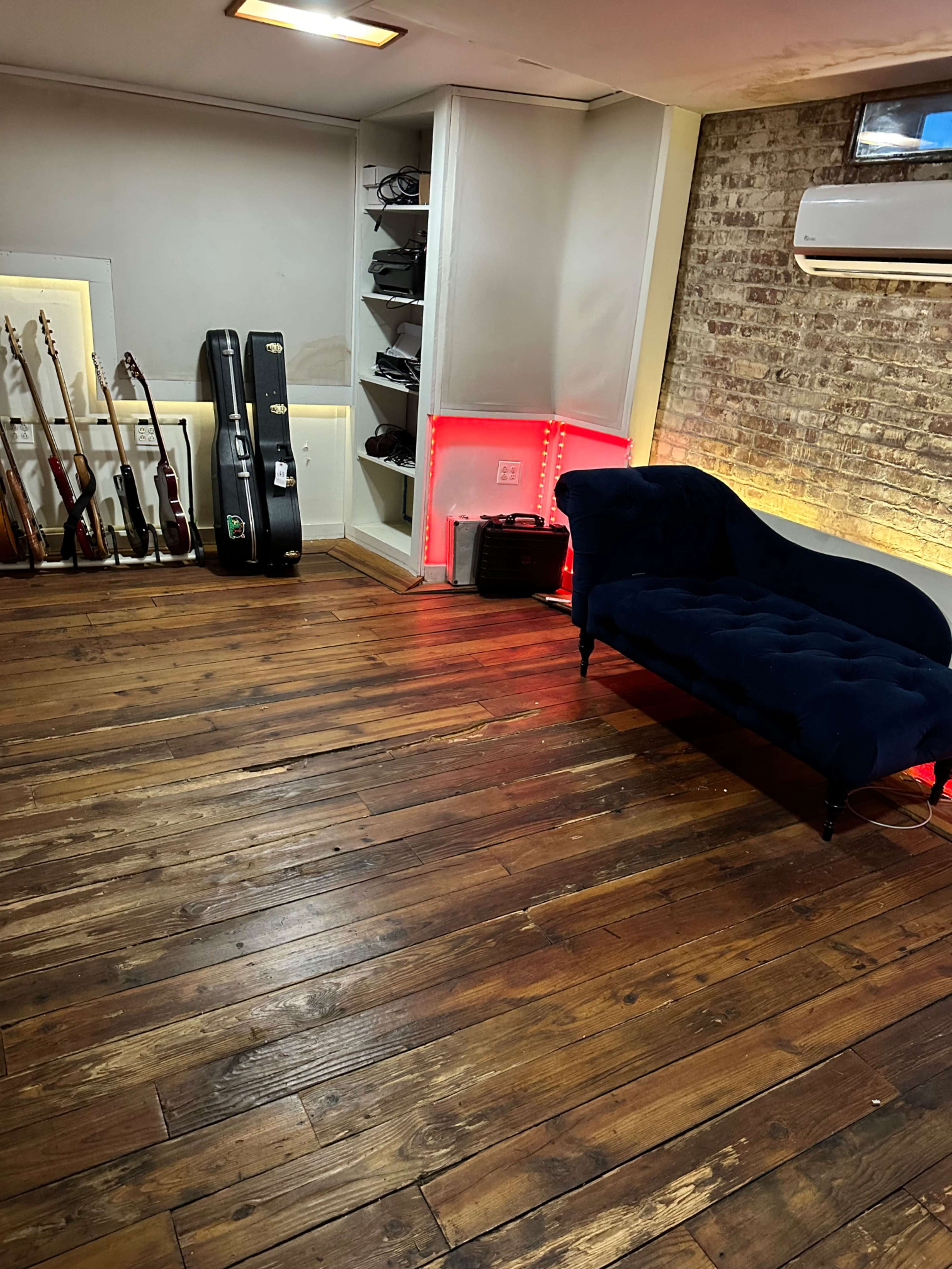 The image shows a room with wooden floorboards, a dark blue couch, and multiple guitars displayed against a wall with ambient lighting.