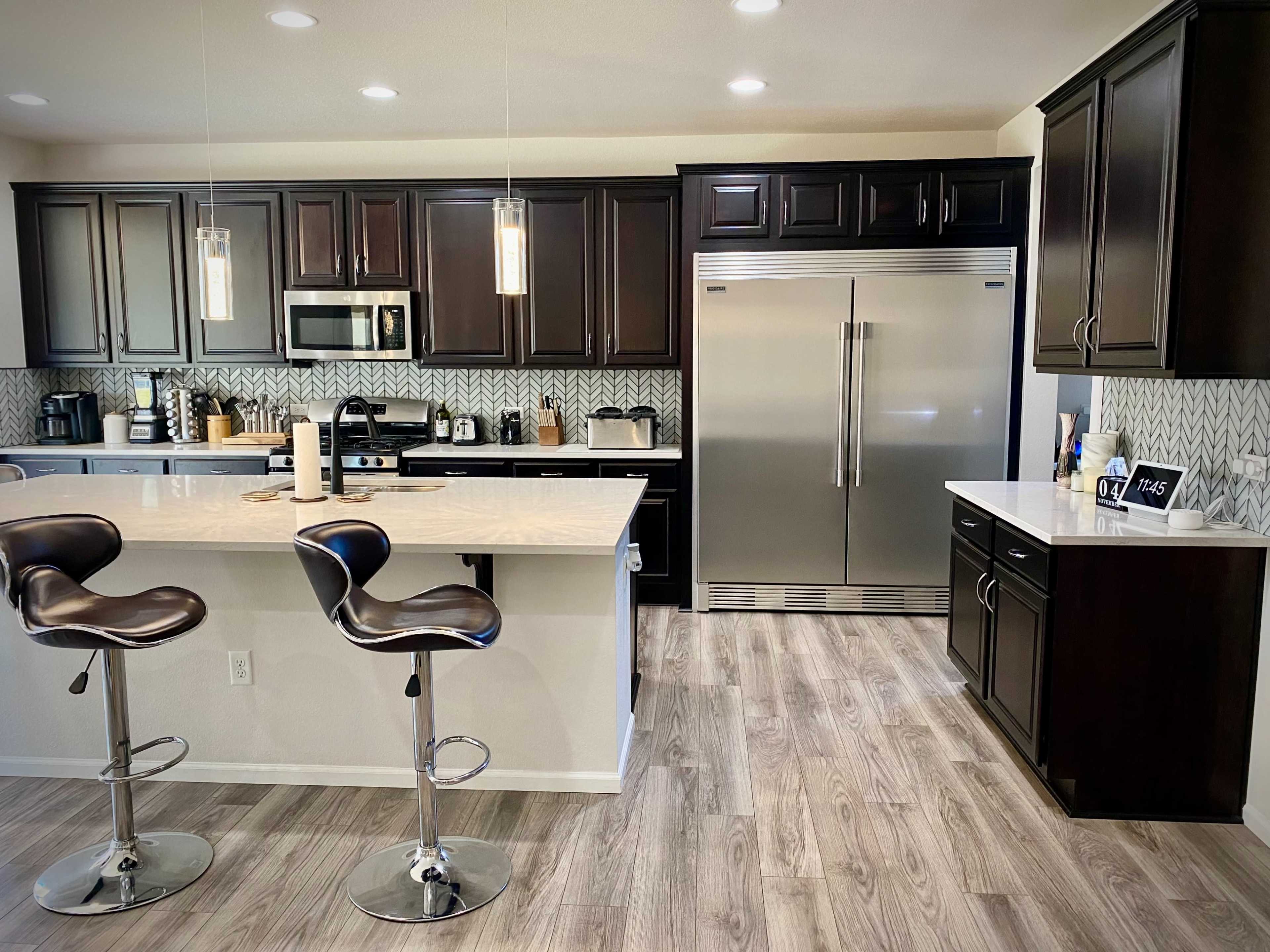 A modern kitchen with dark wood cabinetry, stainless steel appliances, and a central island featuring two bar stools.
