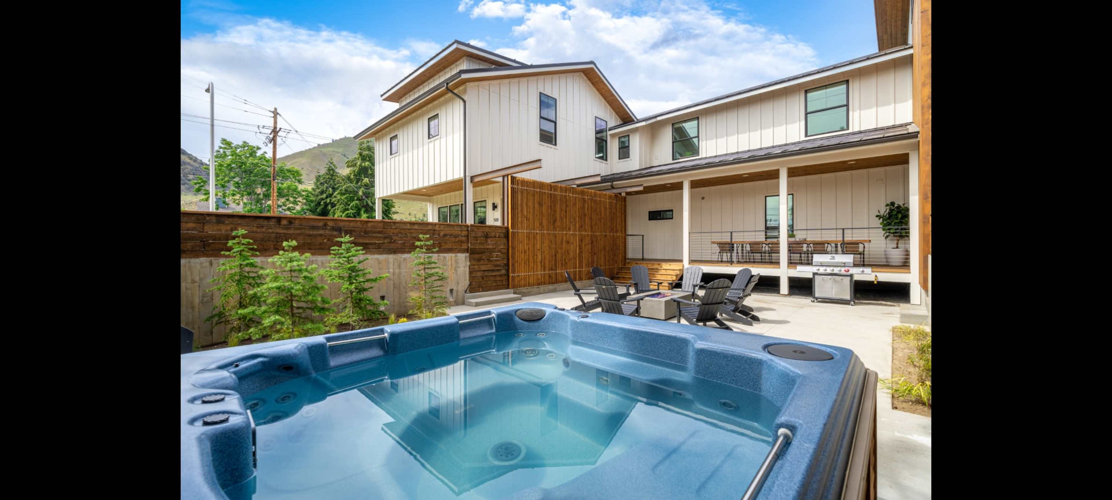 A hot tub is positioned in a private courtyard surrounded by modern buildings with outdoor seating and a grill area.