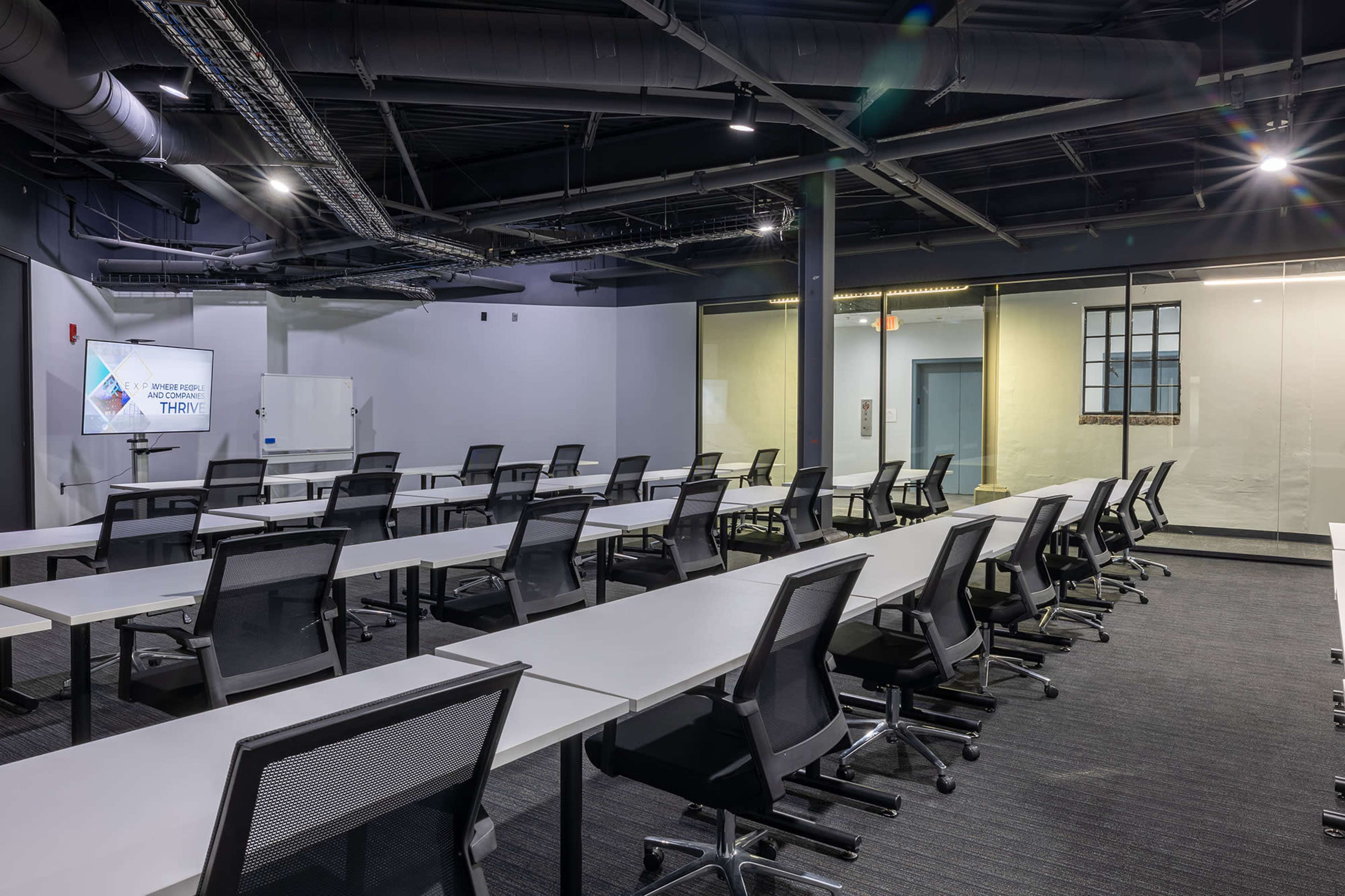 The image shows a modern, well-lit conference room with multiple rows of tables and chairs arranged for a meeting.