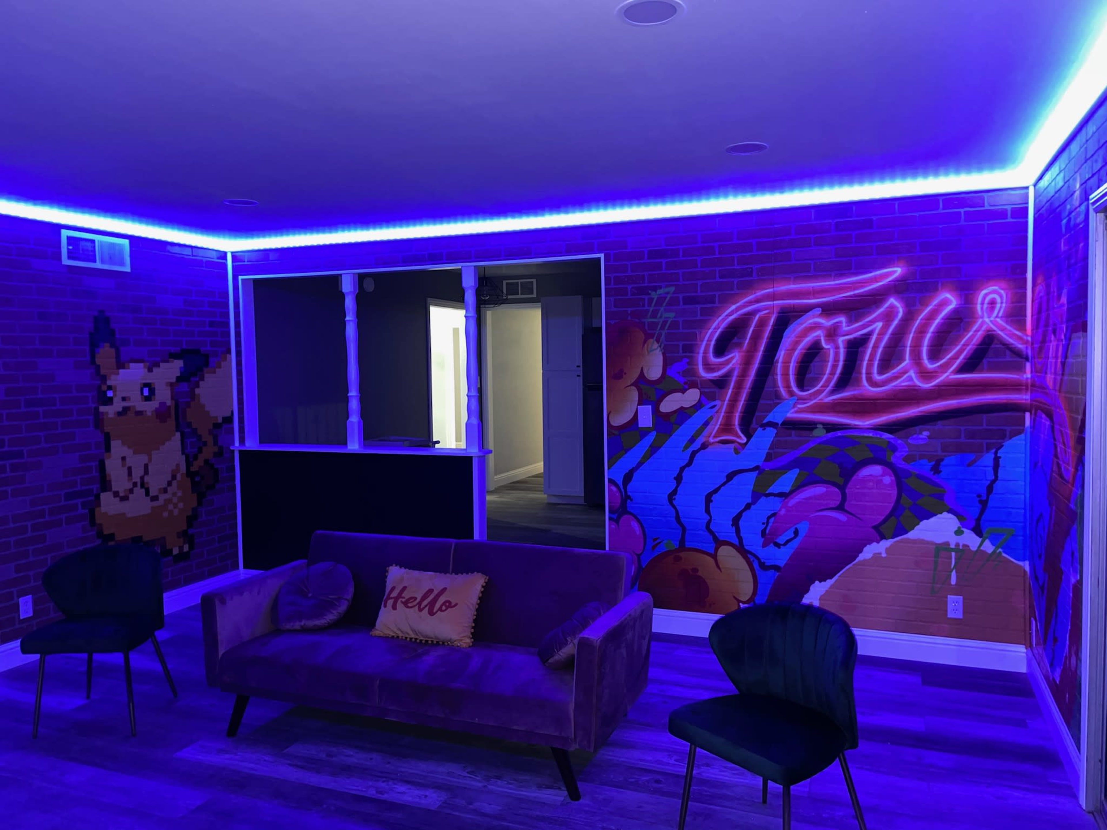 The room features colorful pixel art murals, including a Pikachu, with purple ambient lighting and a sofa in front of a brick wall.