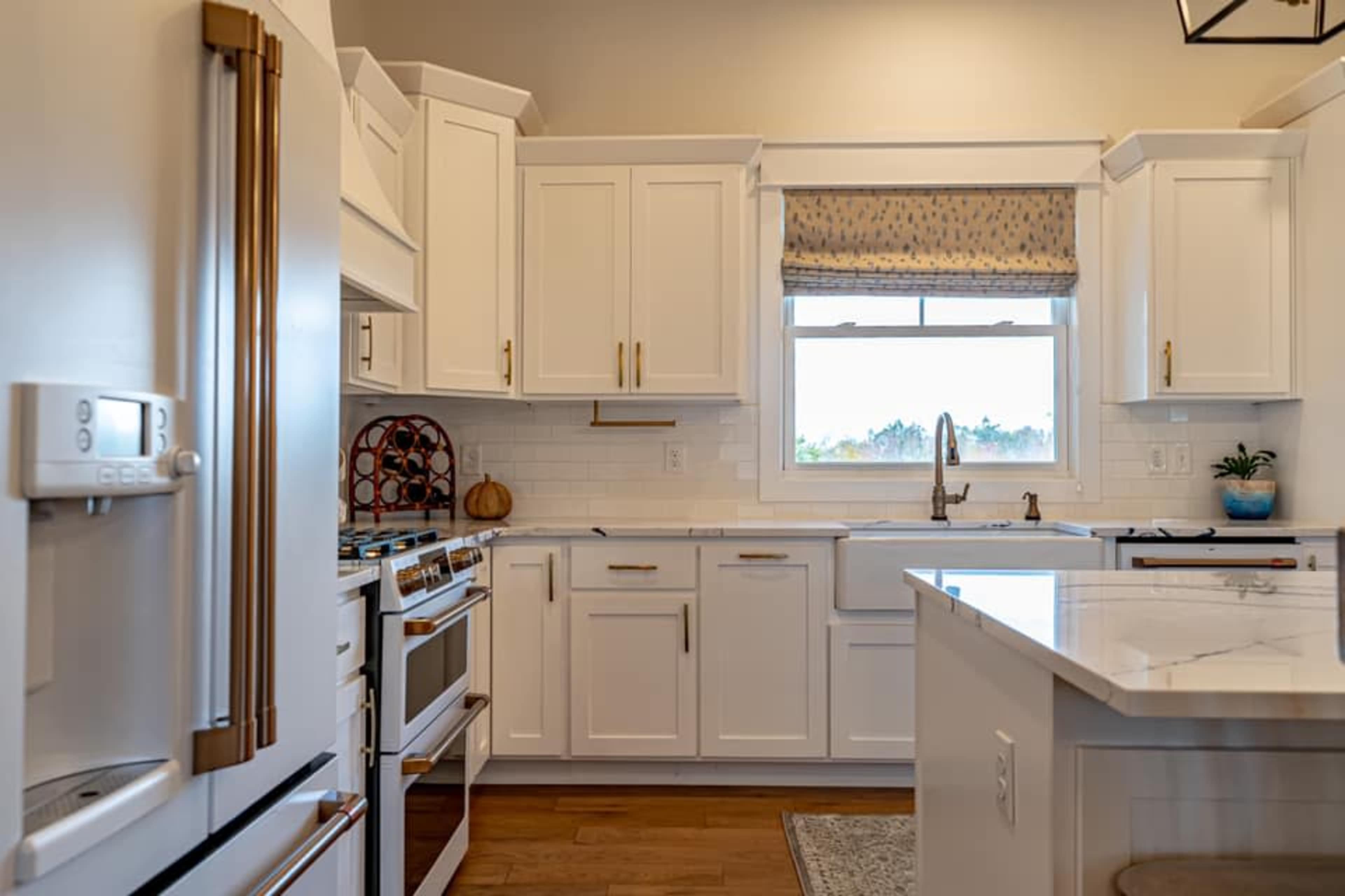A modern kitchen with white cabinetry, a marble countertop, and stainless steel appliances.