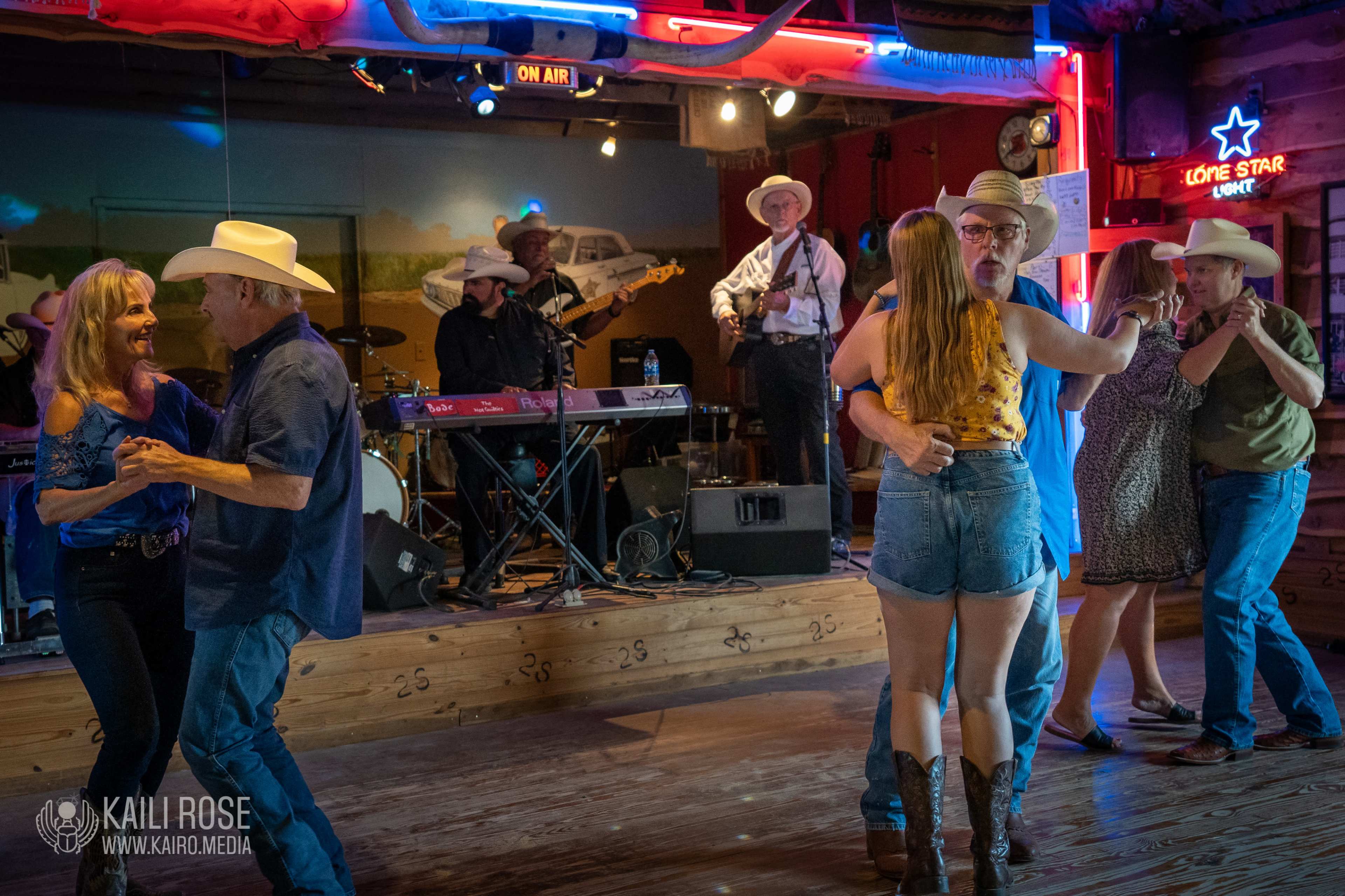 A lively country dance event takes place indoors, with people dancing to a live band playing on stage.