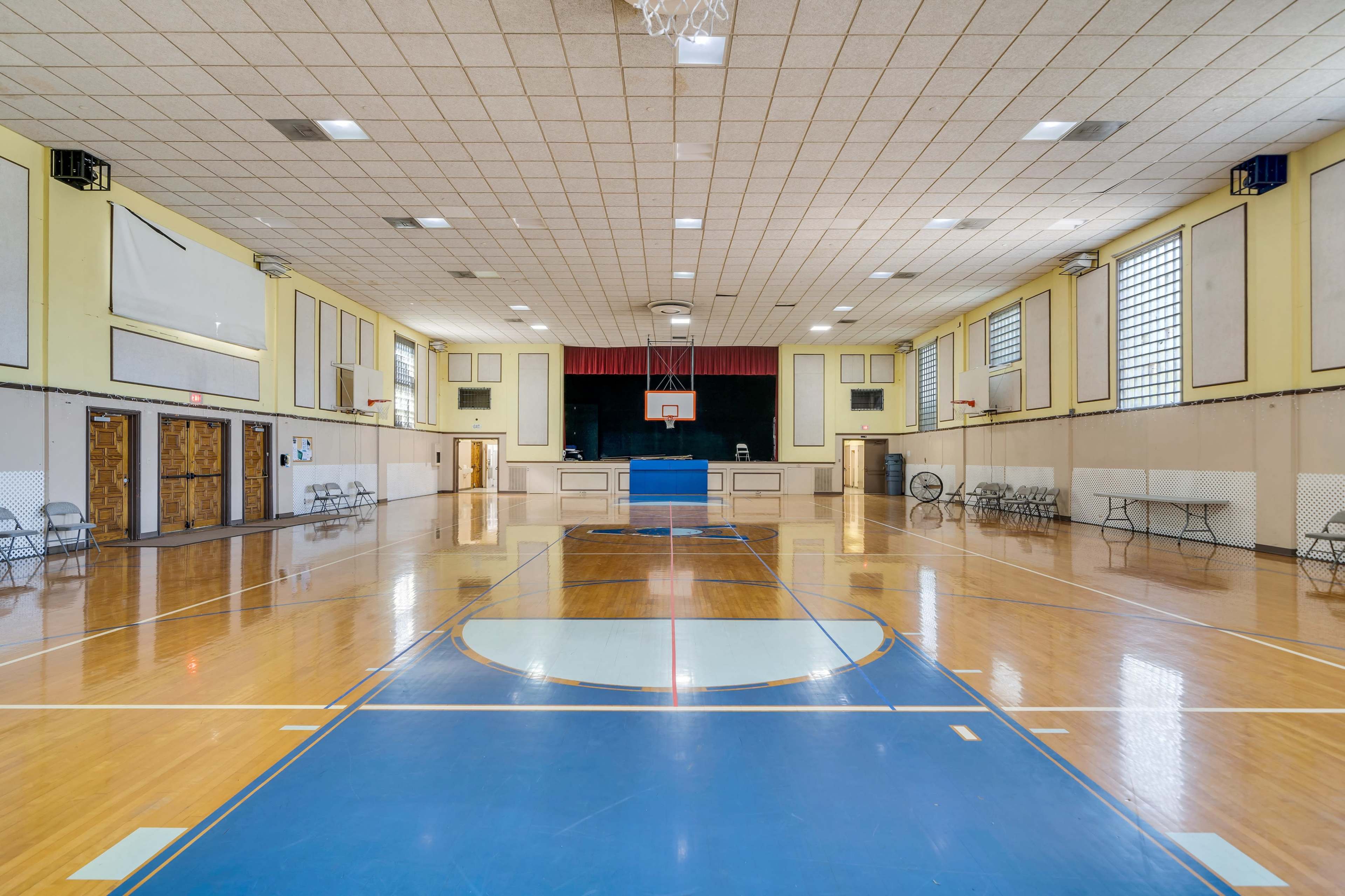 A spacious indoor gymnasium with basketball courts, wooden floors, and bleachers along the sides.