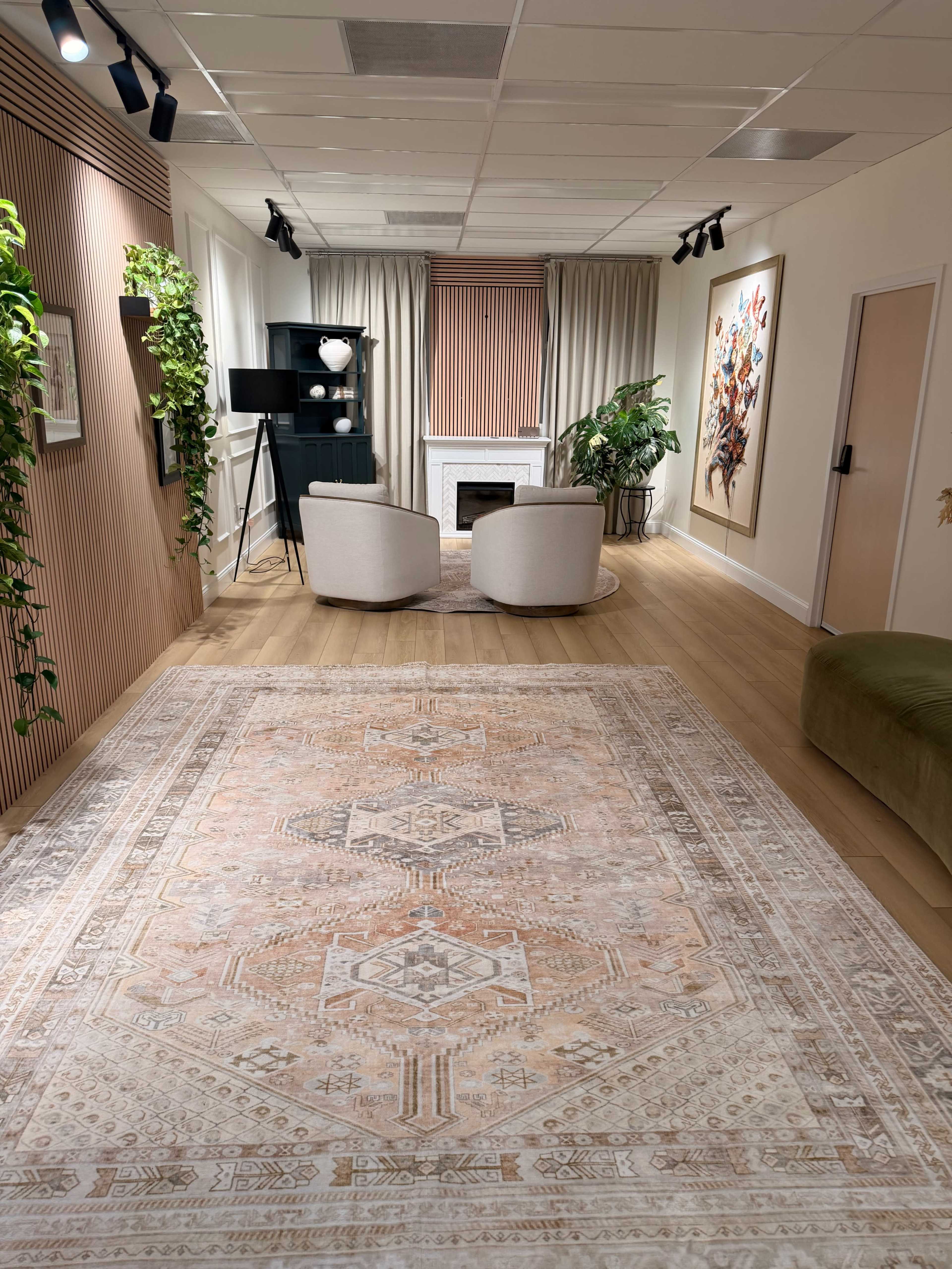 The image shows a modern interior room featuring two armchairs, a decorative rug, a fireplace, and plants, with soft lighting and neutral-colored walls.