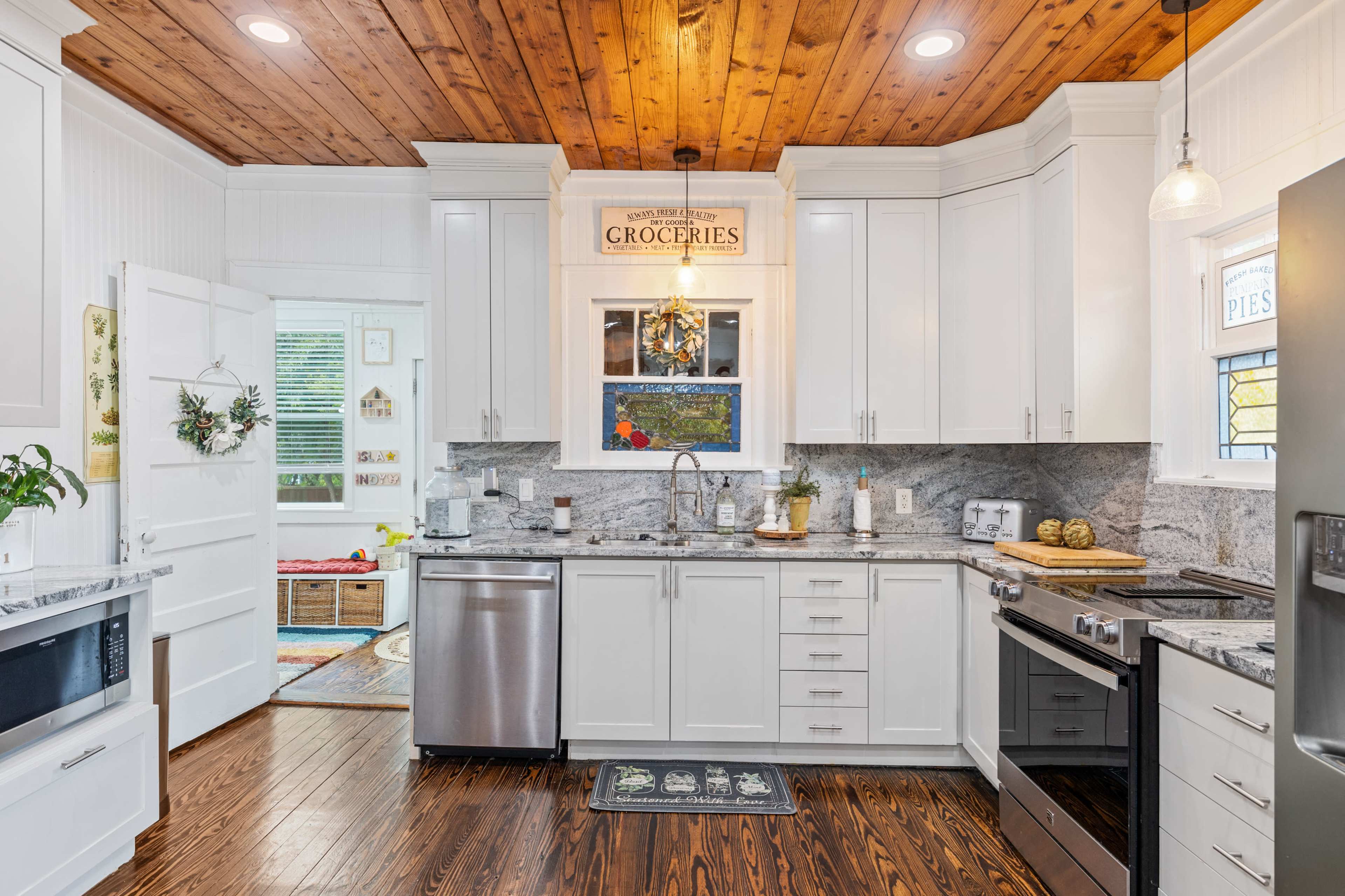 The image shows a modern kitchen with white cabinetry, stainless steel appliances, and a wooden ceiling.