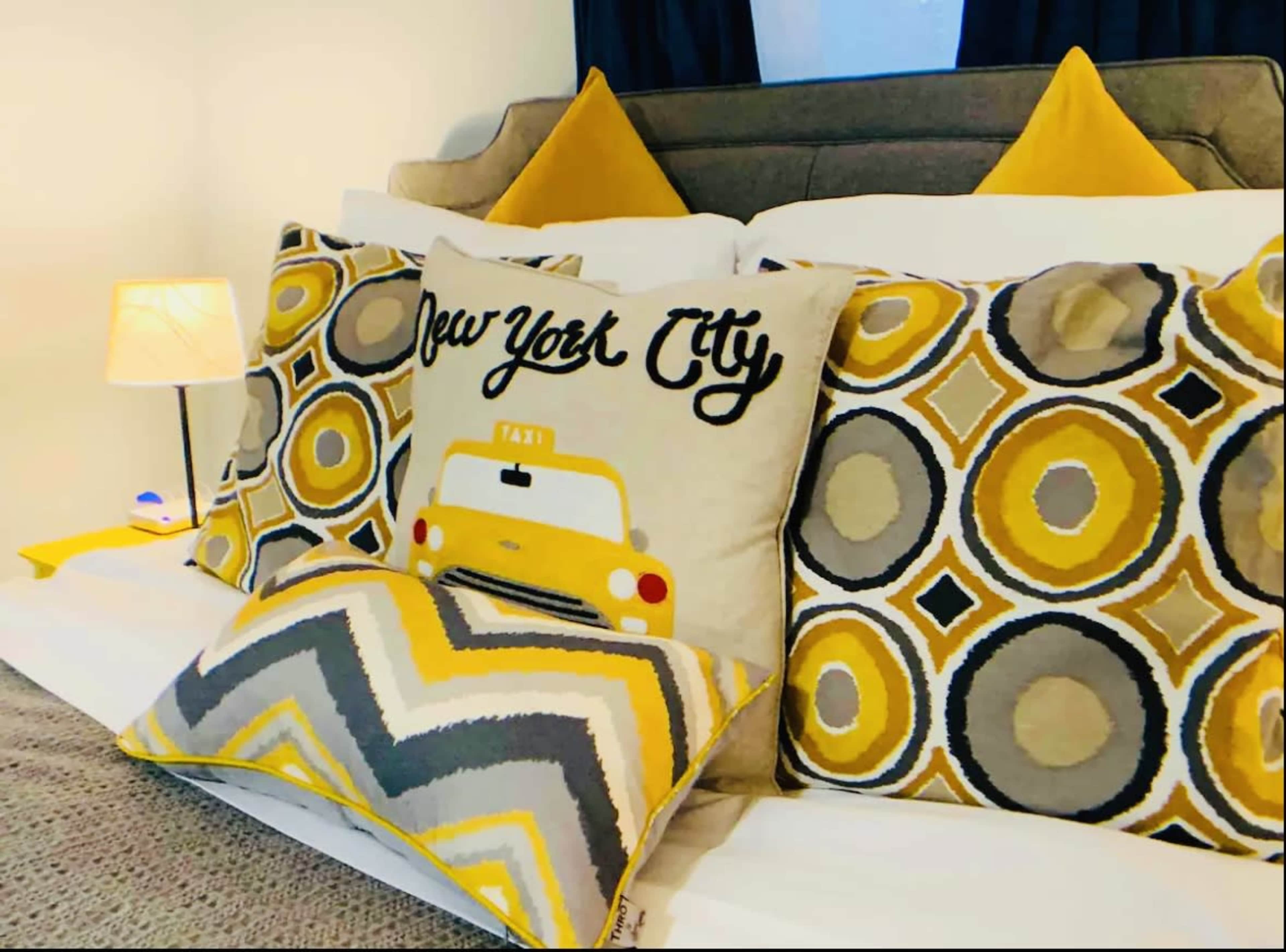 A cozy bed adorned with decorative pillows featuring a taxi motif and circular patterns in yellow and gray tones.