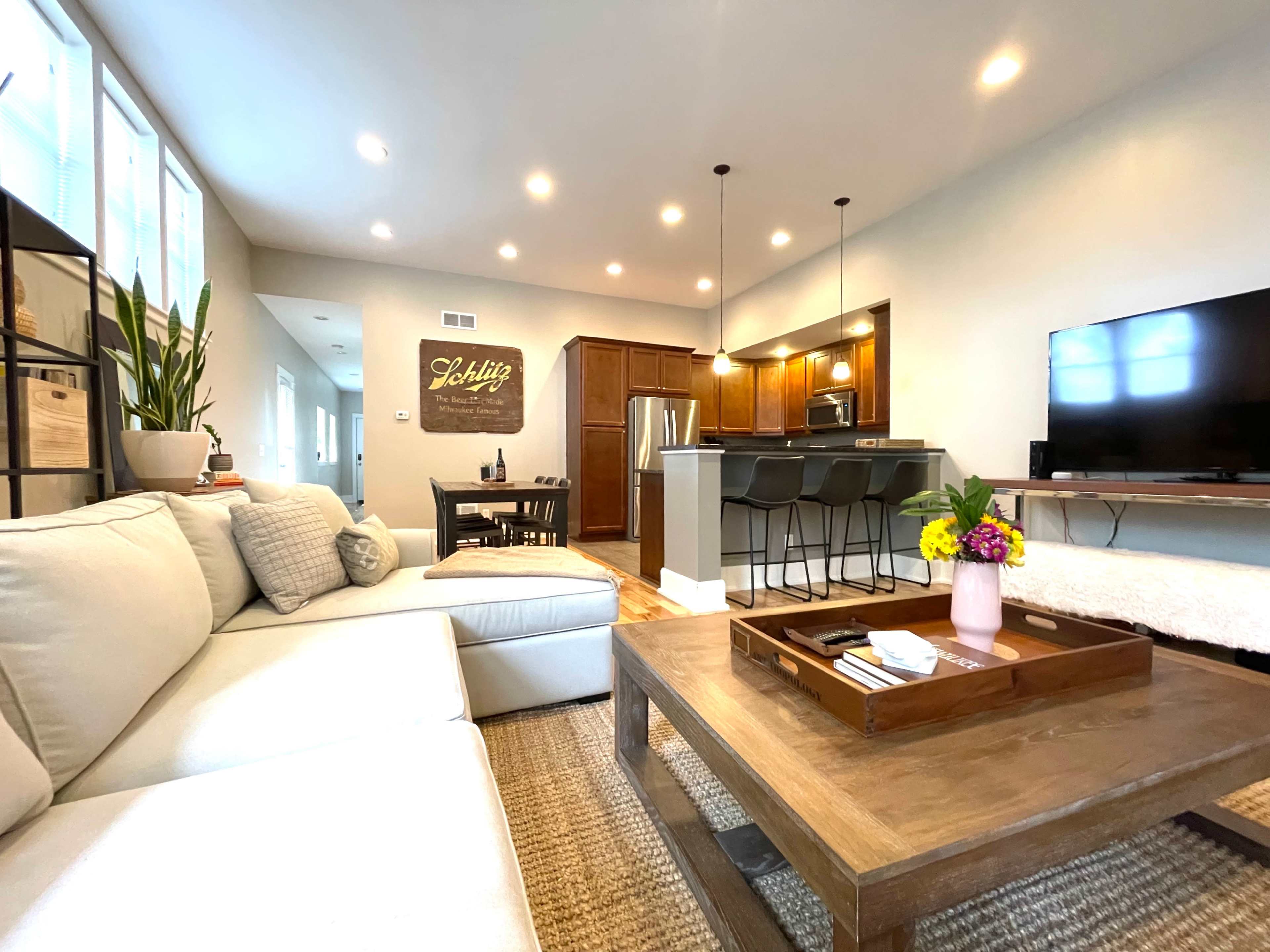 A modern living room with a sectional sofa, a wooden coffee table, a dining area, and a kitchen in the background.