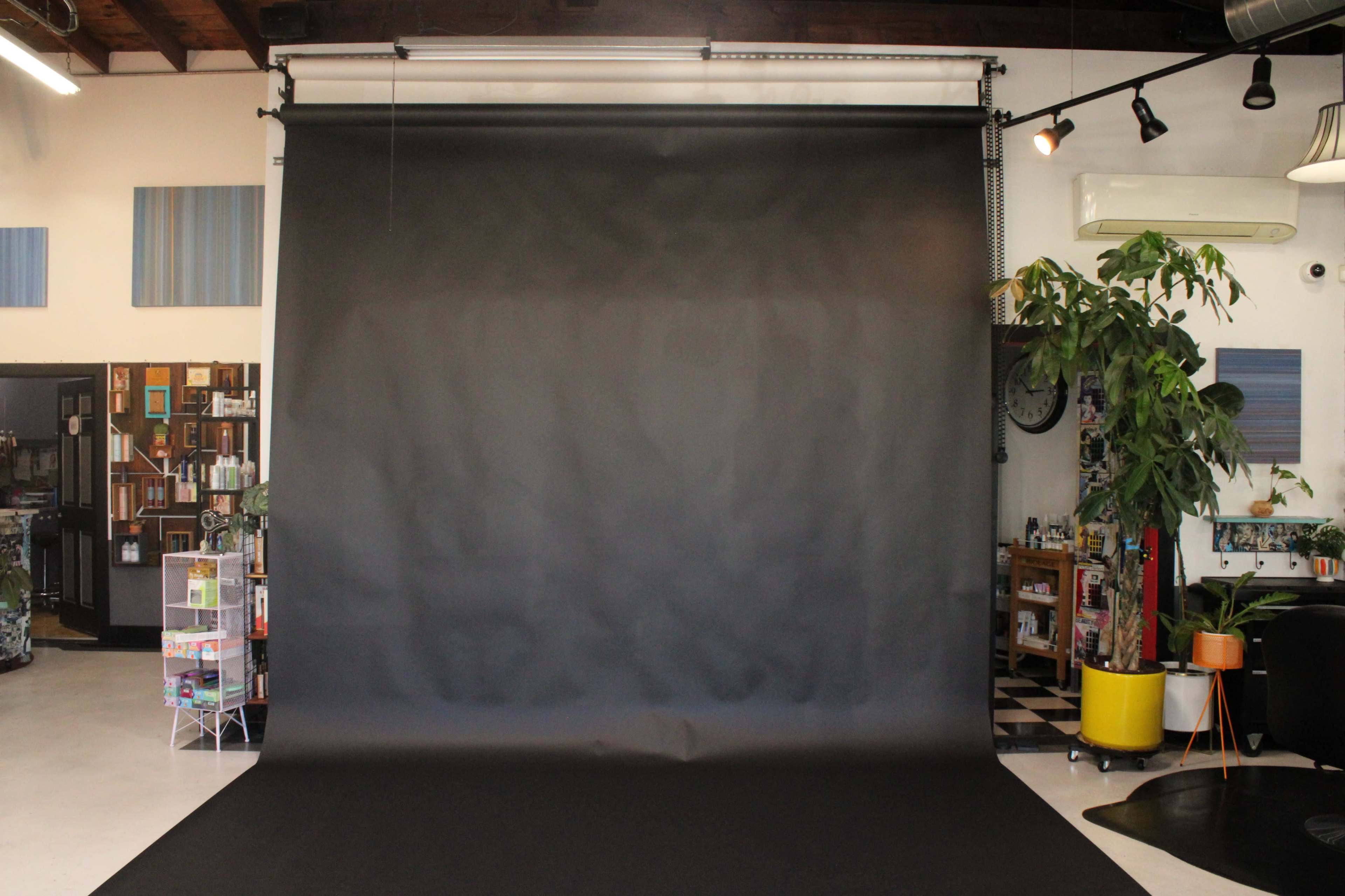 The image shows an empty photography studio featuring a large black backdrop and a variety of furniture and decor in the background.