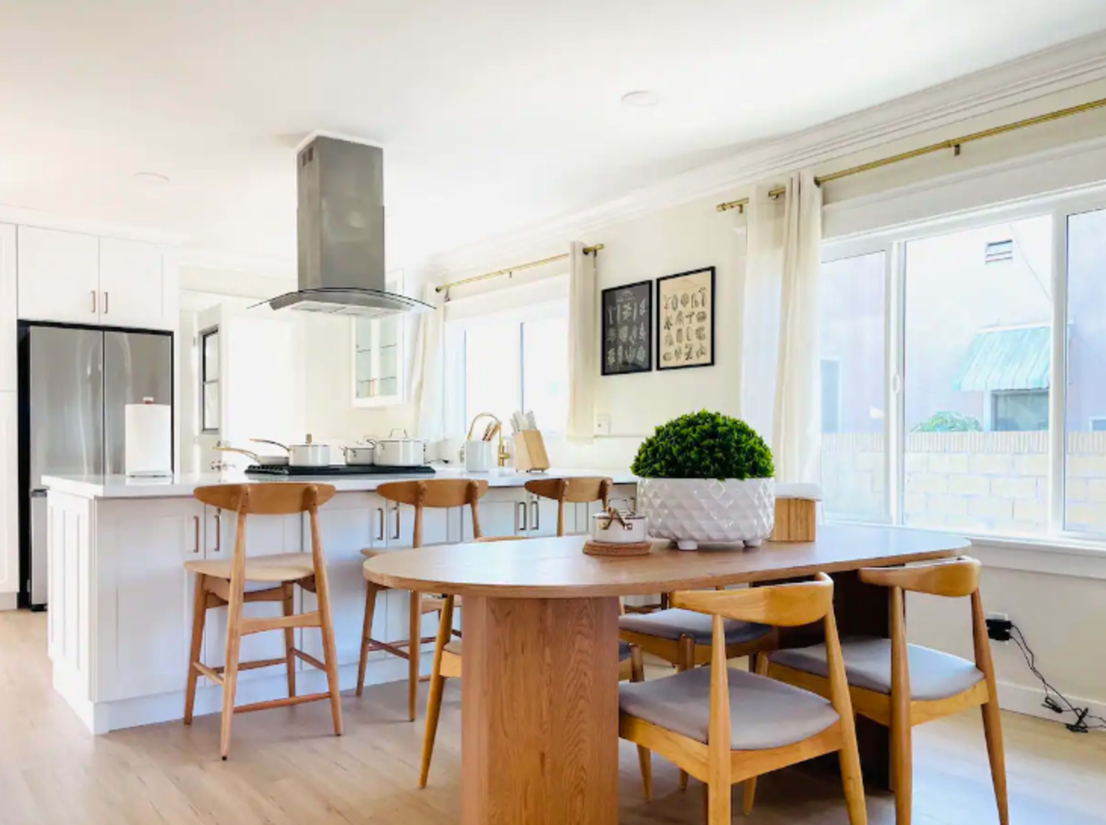 A modern kitchen with a central island, bar stools, and a round dining table adjacent to large windows.