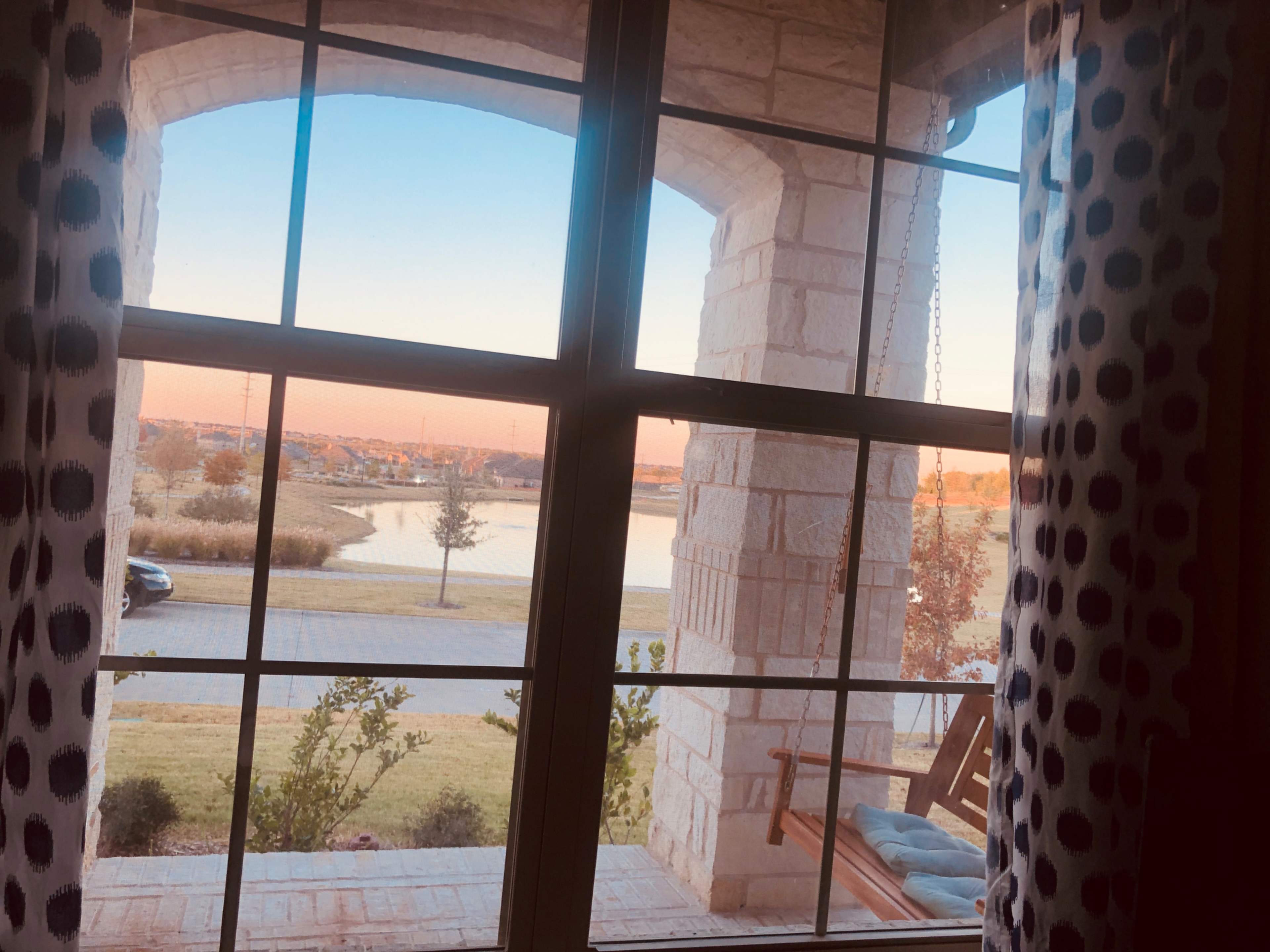 The image shows a view through a window, featuring a landscape with a pond, grass, and a parked car under a clear sky at sunset.