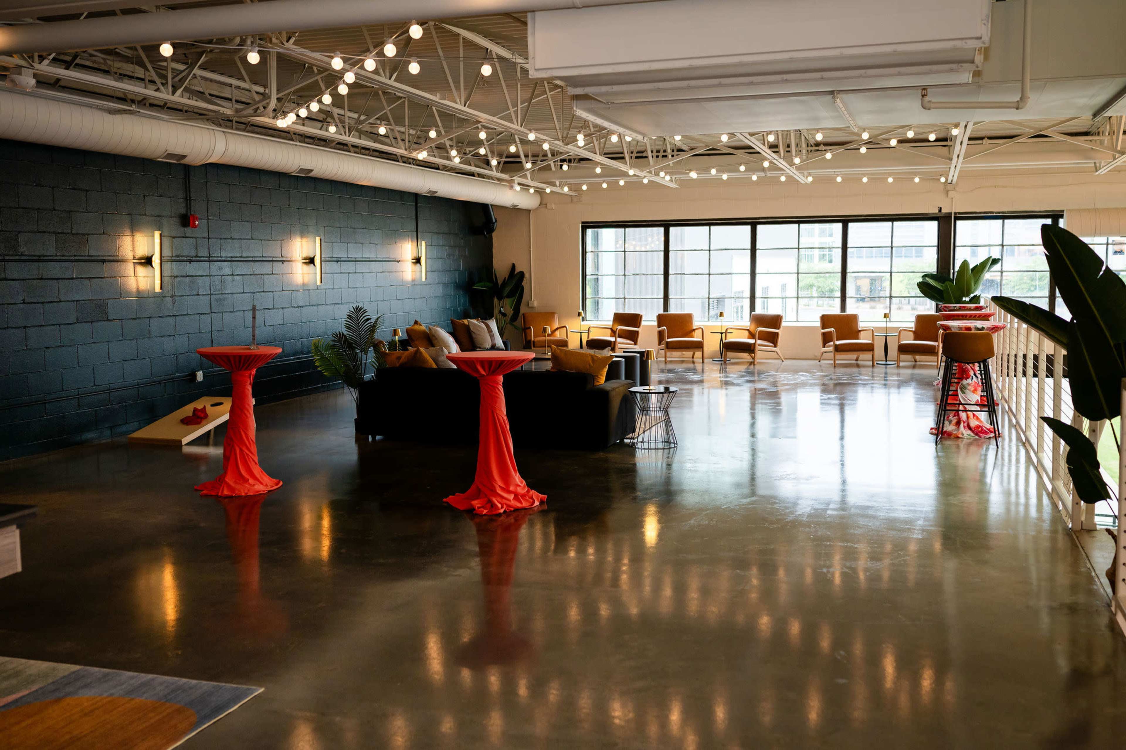 The image shows a modern, open lounge area with a polished concrete floor, colorful furniture, and bright lighting fixtures.