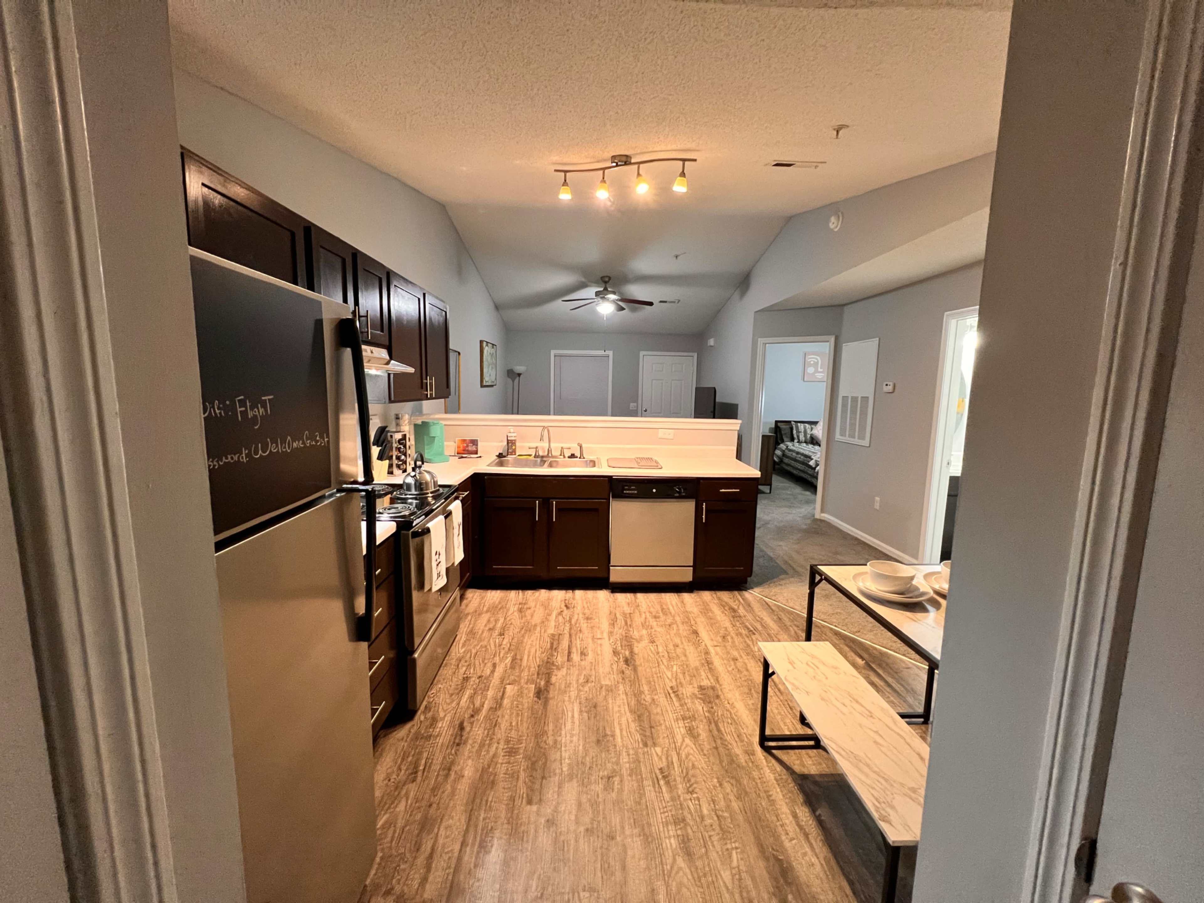 A modern kitchen with dark wooden cabinets, stainless steel appliances, and a central island, viewed from a doorway.