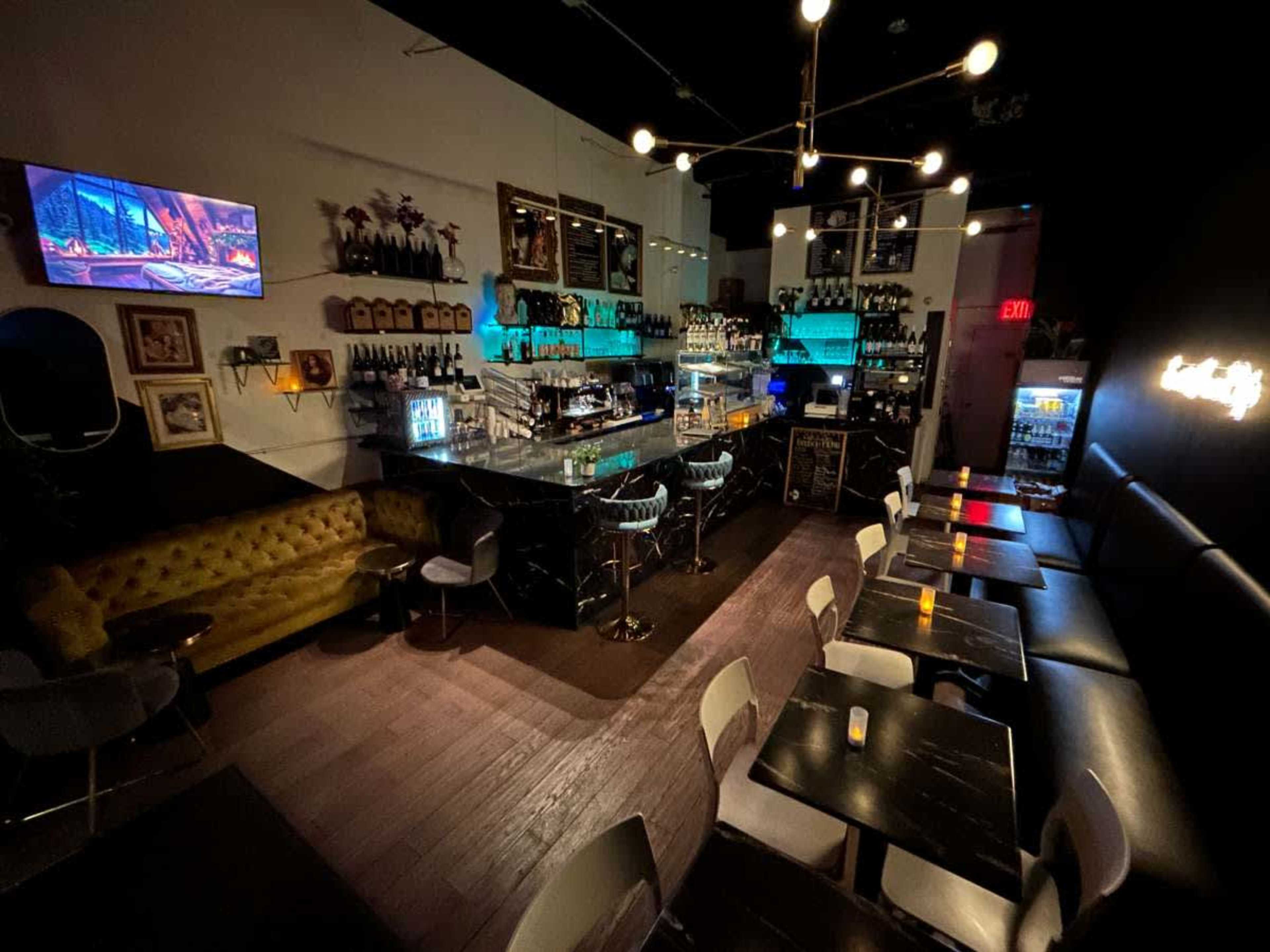 A dimly lit bar interior featuring a black marble counter, shelves stocked with bottles, and upholstered seating along the walls.