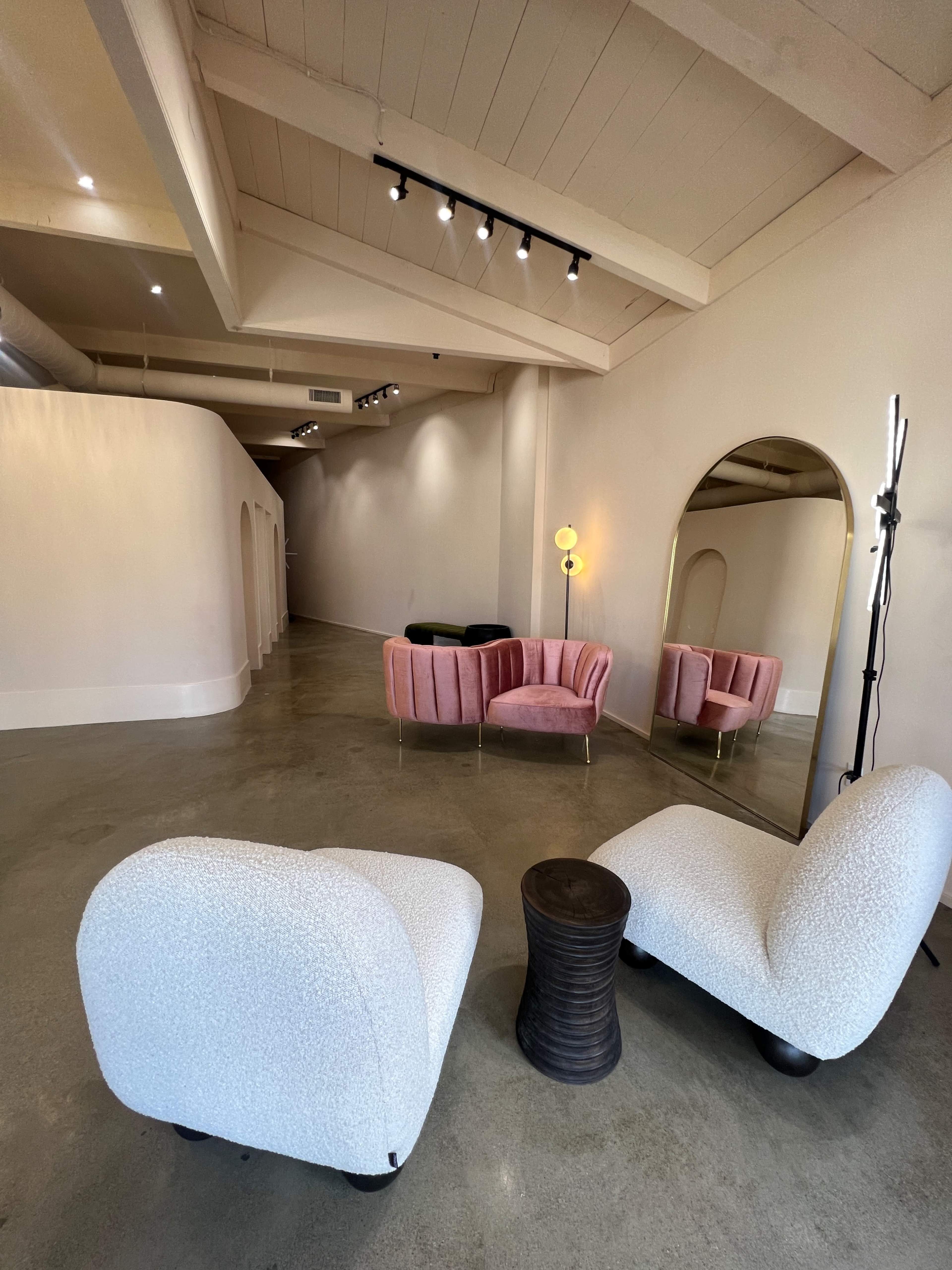 A modern interior space featuring two plush chairs, a small side table, and a curved hallway with a large mirror and soft lighting.