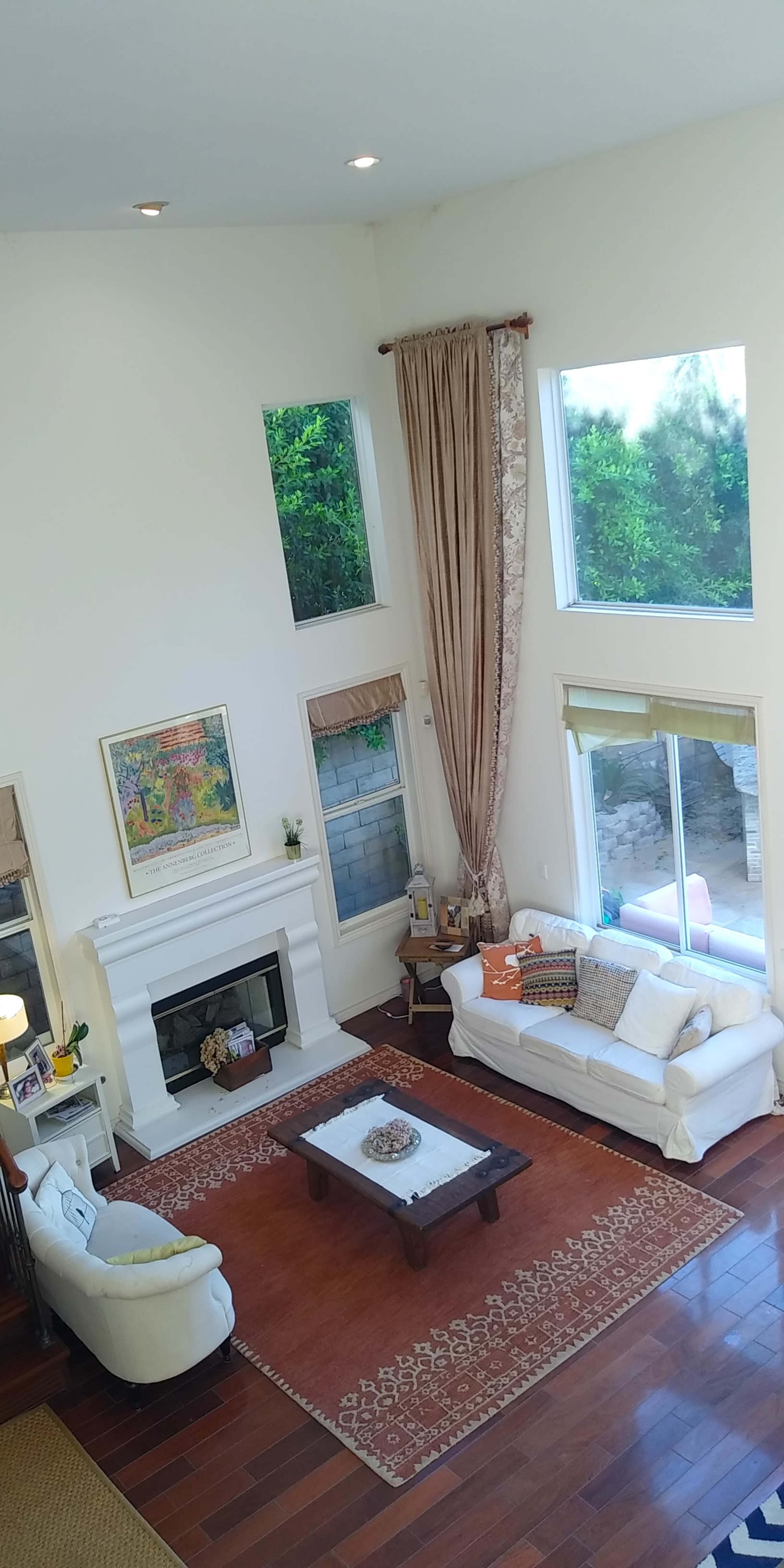 A bright living room with large windows, a fireplace, and two sofas arranged around a coffee table on a patterned rug.