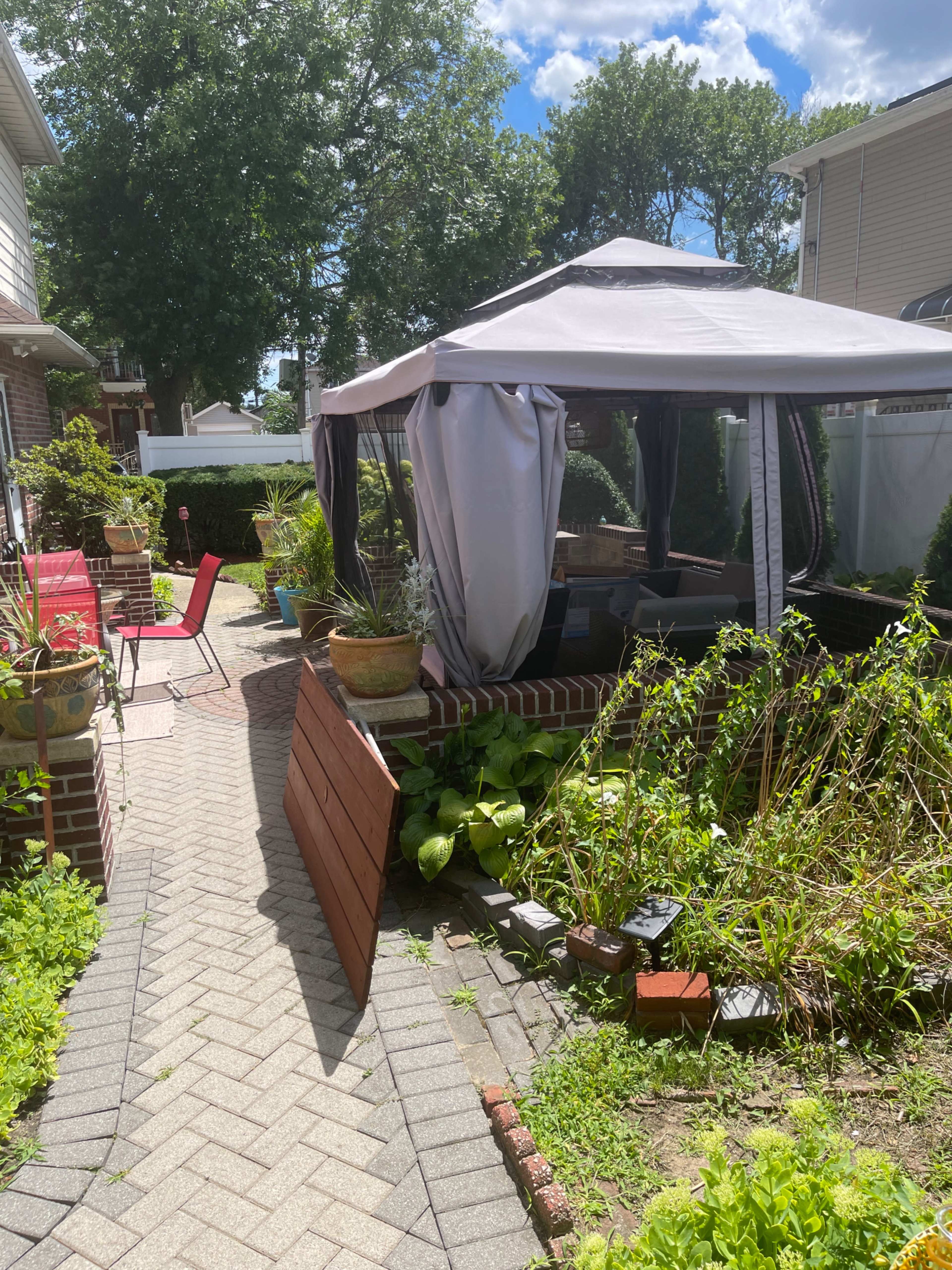 A pathway leads to a gazebo surrounded by potted plants and overgrown garden beds.