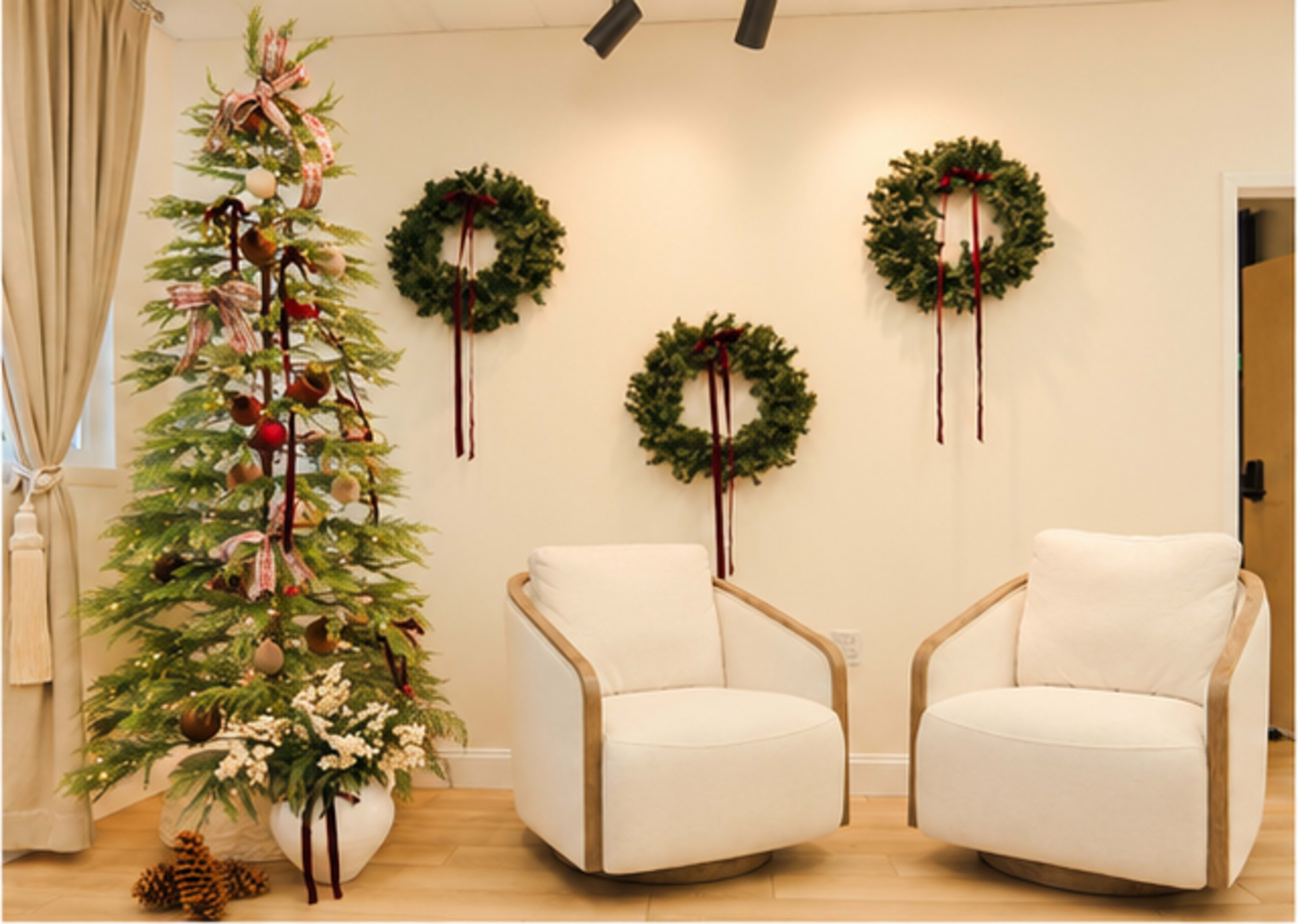 The image shows a cozy interior decorated for the holidays, featuring a Christmas tree adorned with ornaments and adjacent wall wreaths, accompanied by two white armchairs.