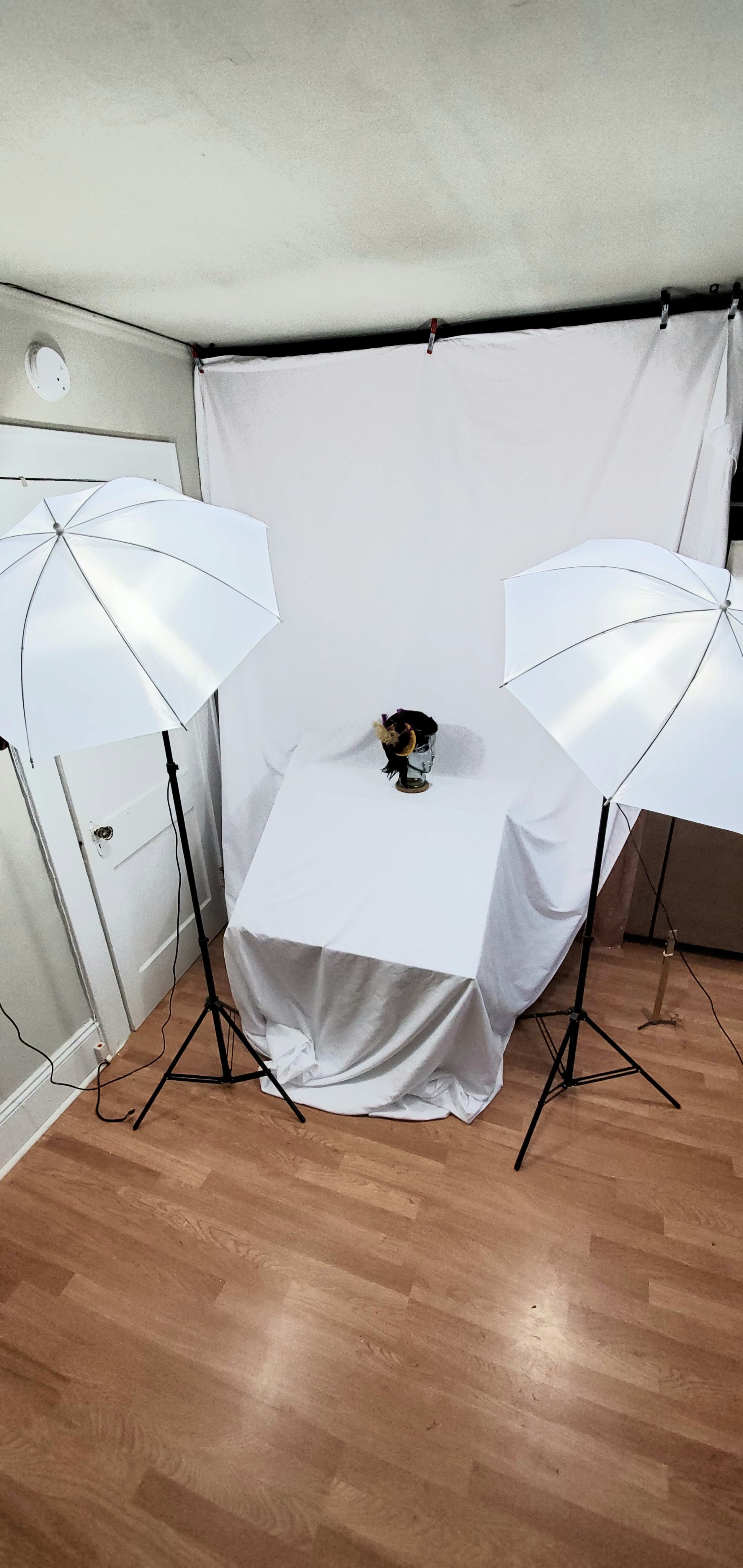 A photography setup in a room, featuring two softbox lights and a white backdrop with a table covered in a white cloth.