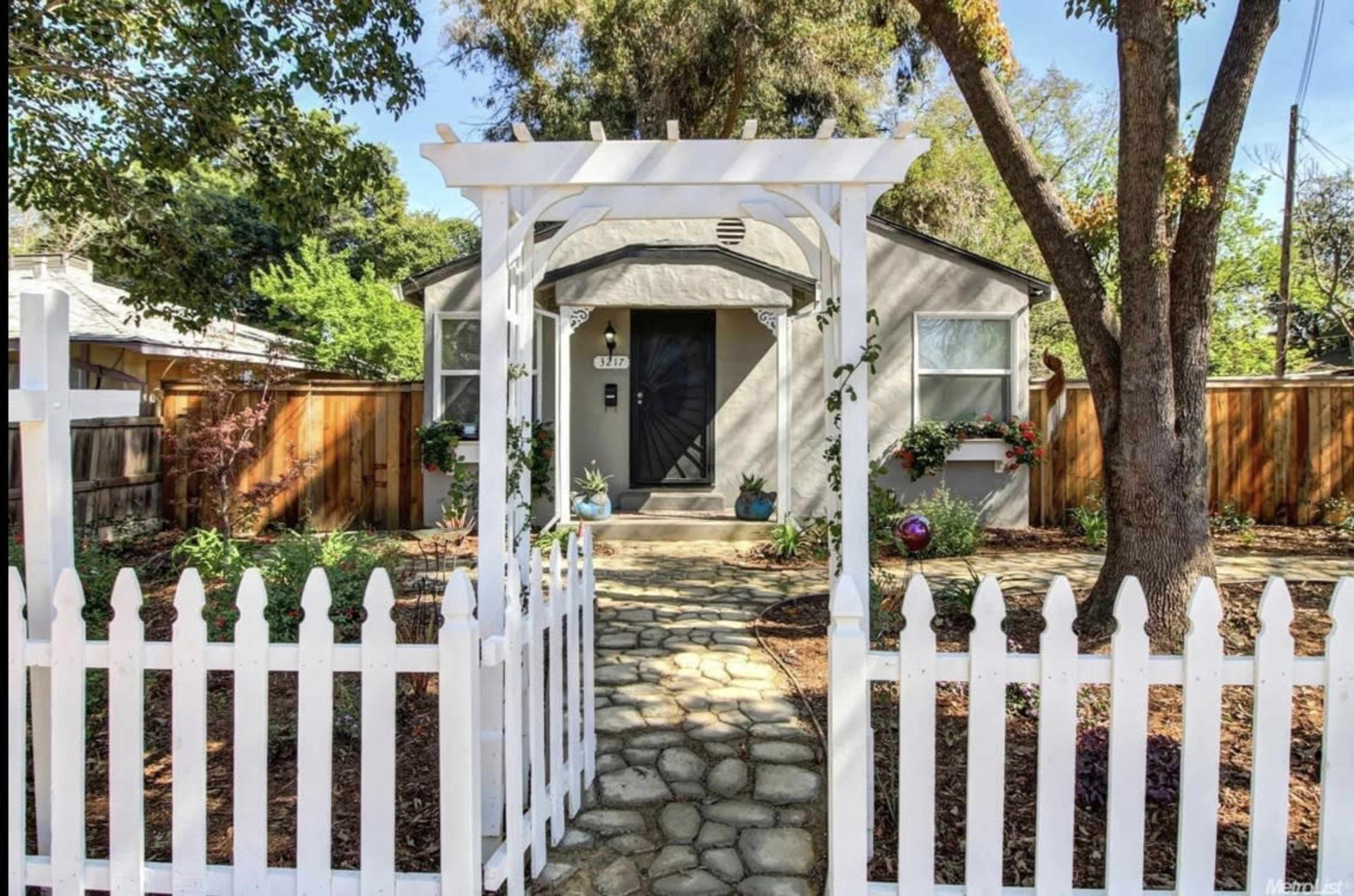A small, gray house with a white picket fence and a stone pathway leading to the front door.