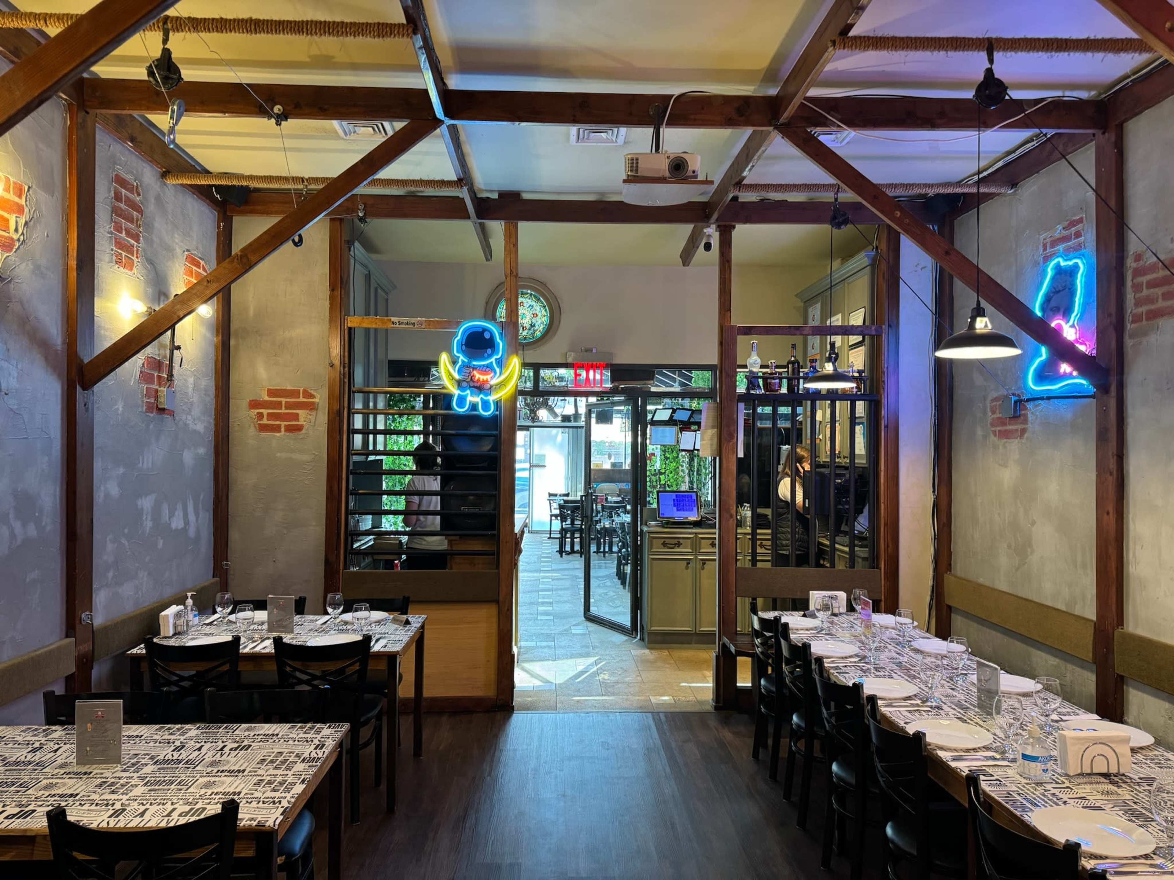 The image shows a modern restaurant interior featuring wooden beams, a long dining table set with white tablecloths, and neon lights on the walls.
