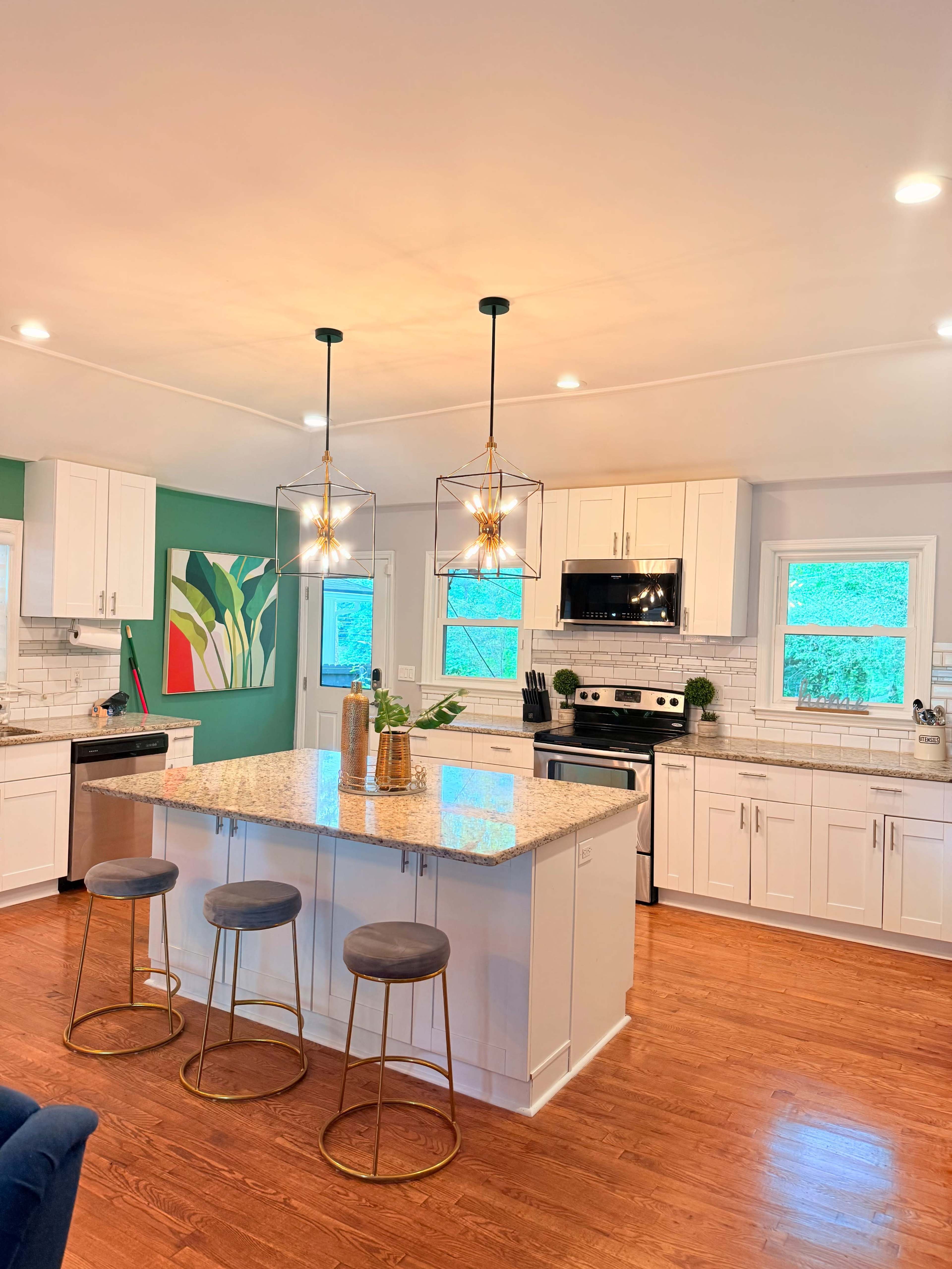 The image shows a modern kitchen featuring white cabinetry, a large island with three bar stools, and pendant lighting above.