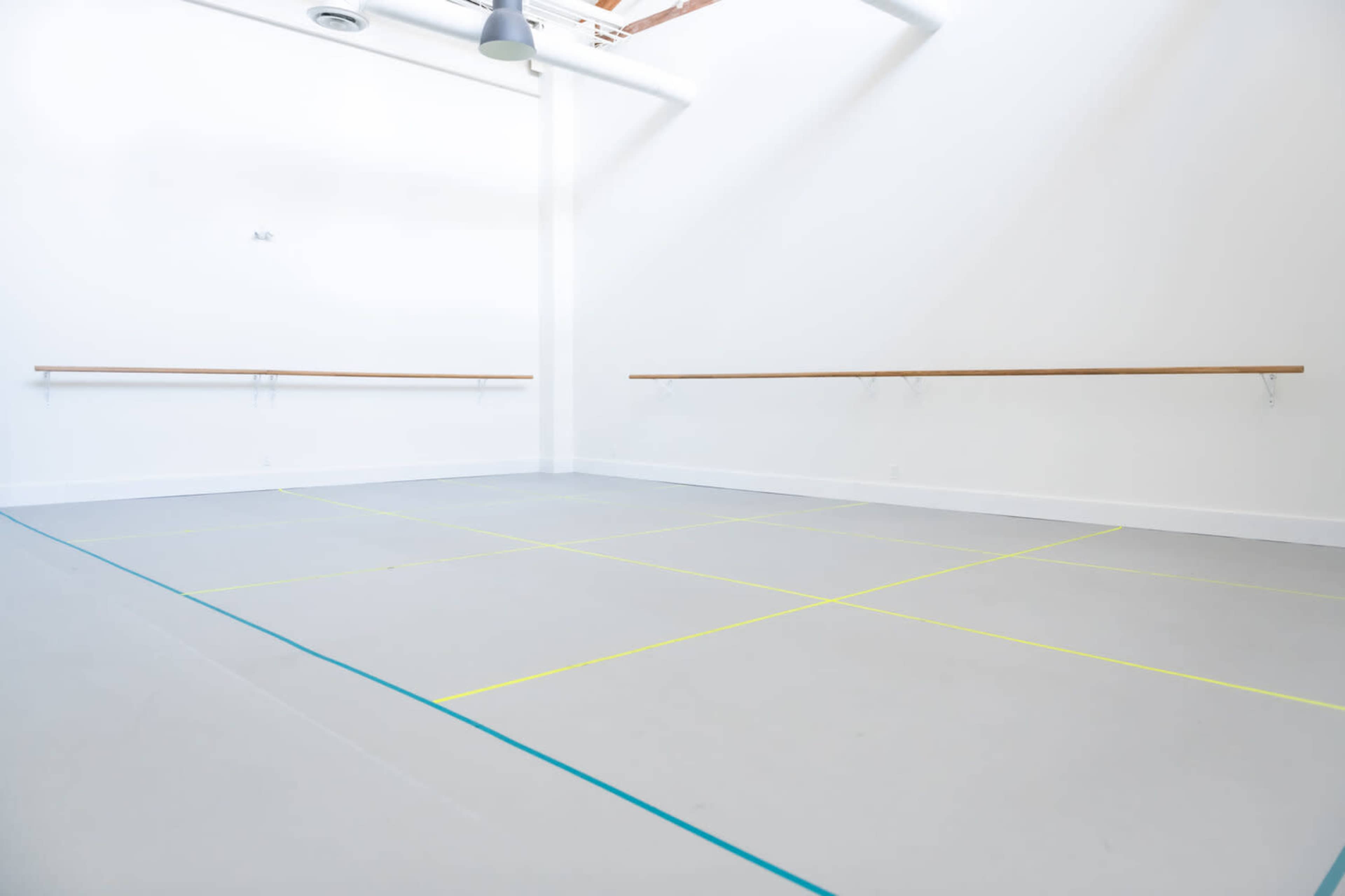 A spacious dance studio with light gray flooring and ballet barres mounted on white walls.