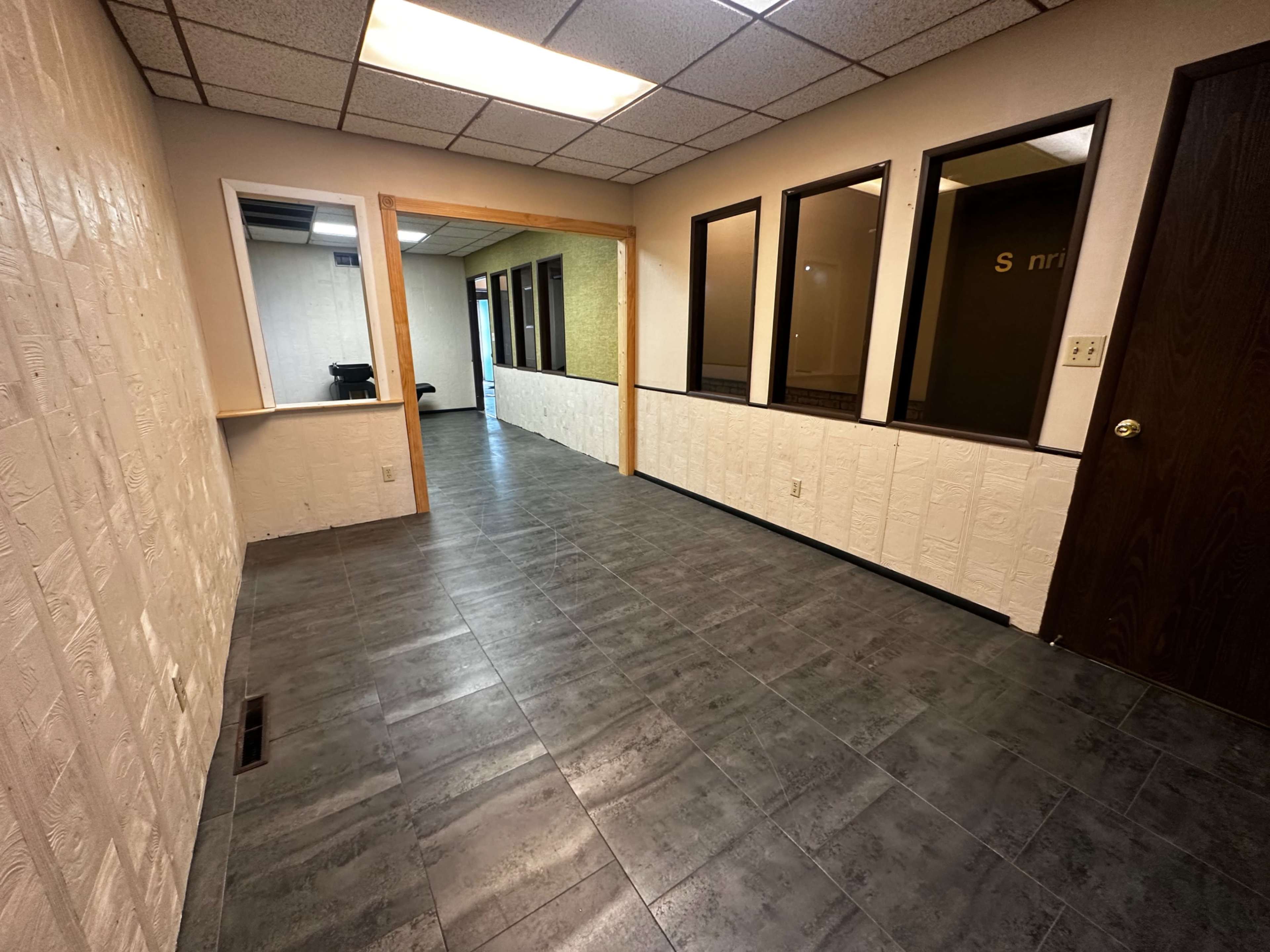 The image shows a hallway in an office building with tiled flooring and access to several rooms on one side.