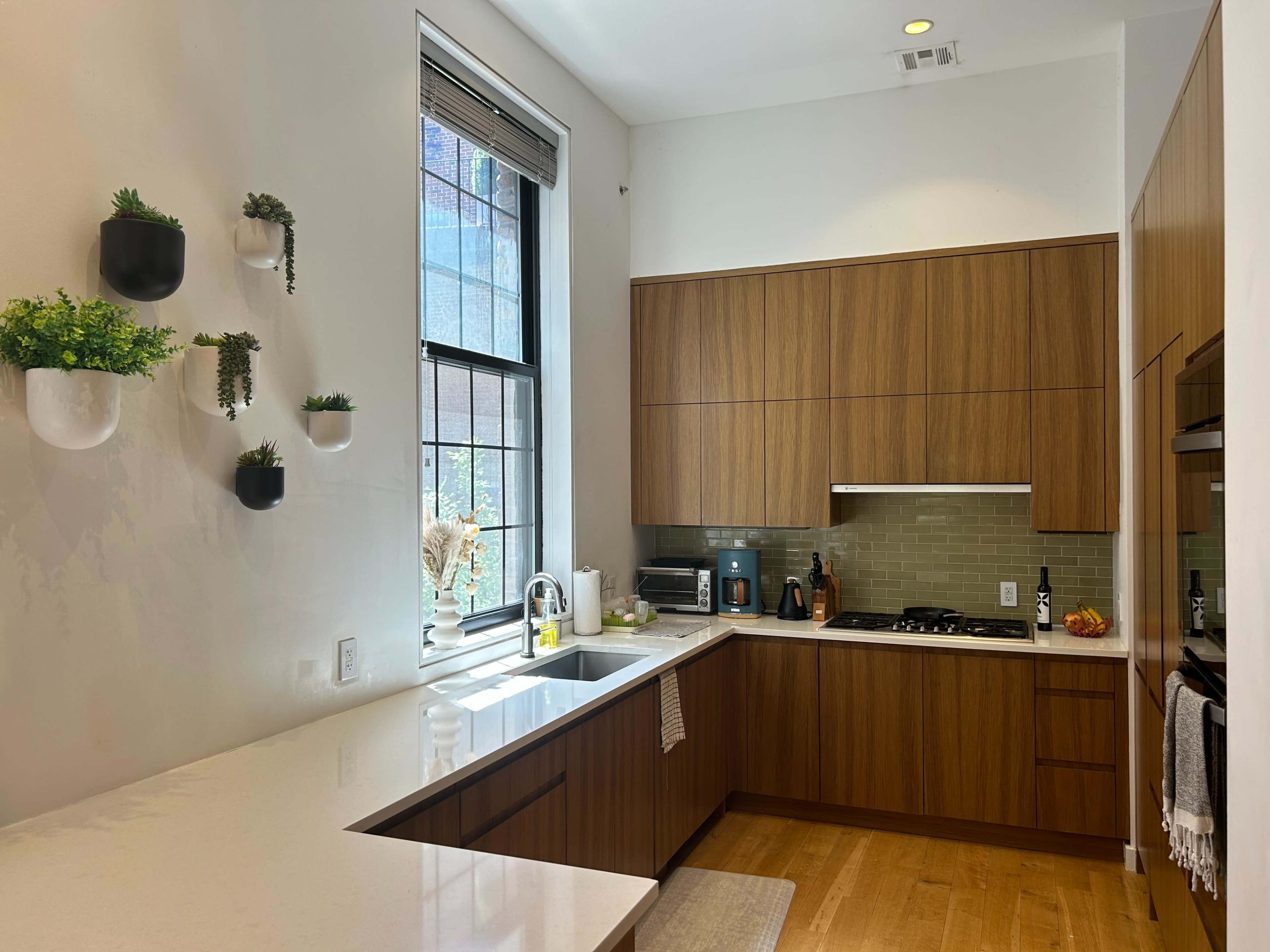 The kitchen features wooden cabinetry, a white countertop, and plants in wall-mounted pots.
