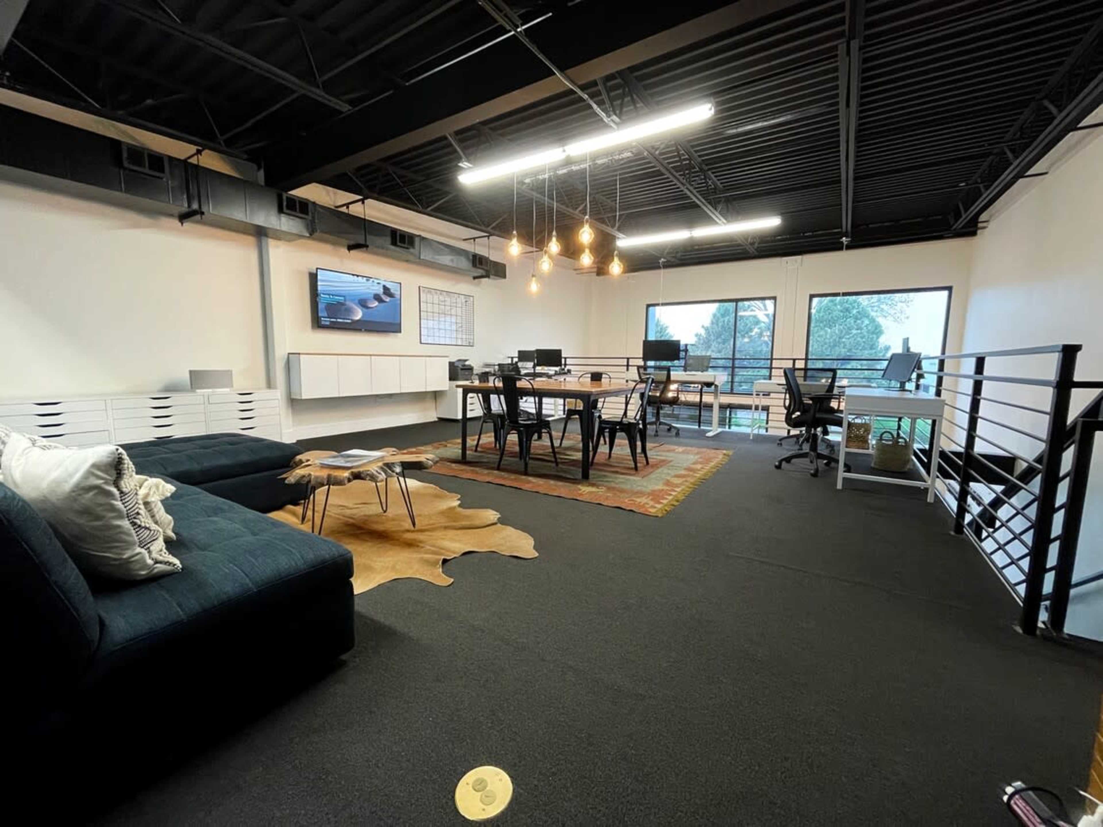 A modern office space with a seating area, a dining table, and large windows overlooking greenery.
