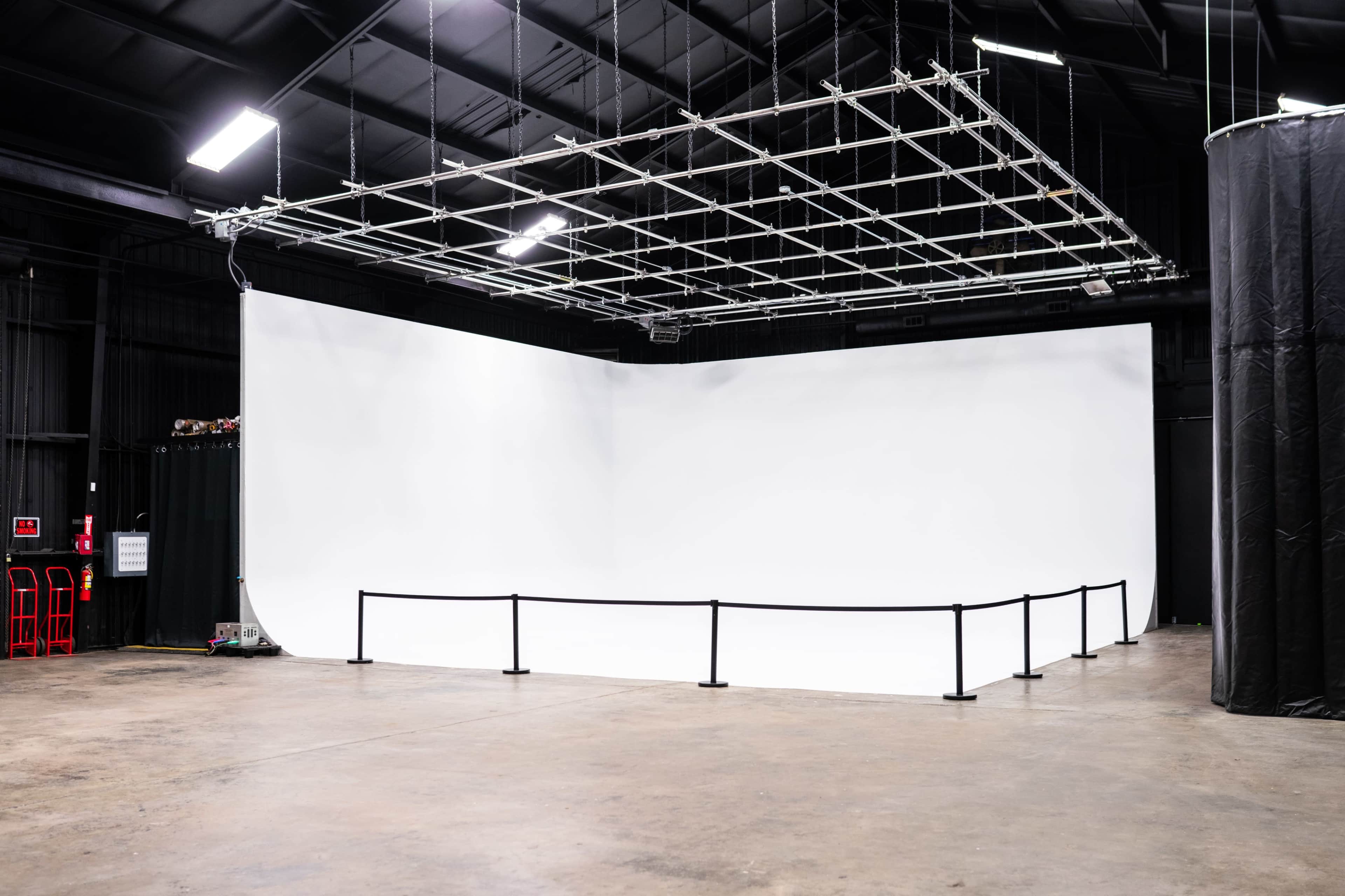 A large, empty studio space with a seamless white backdrop and a grid of overhead lights.