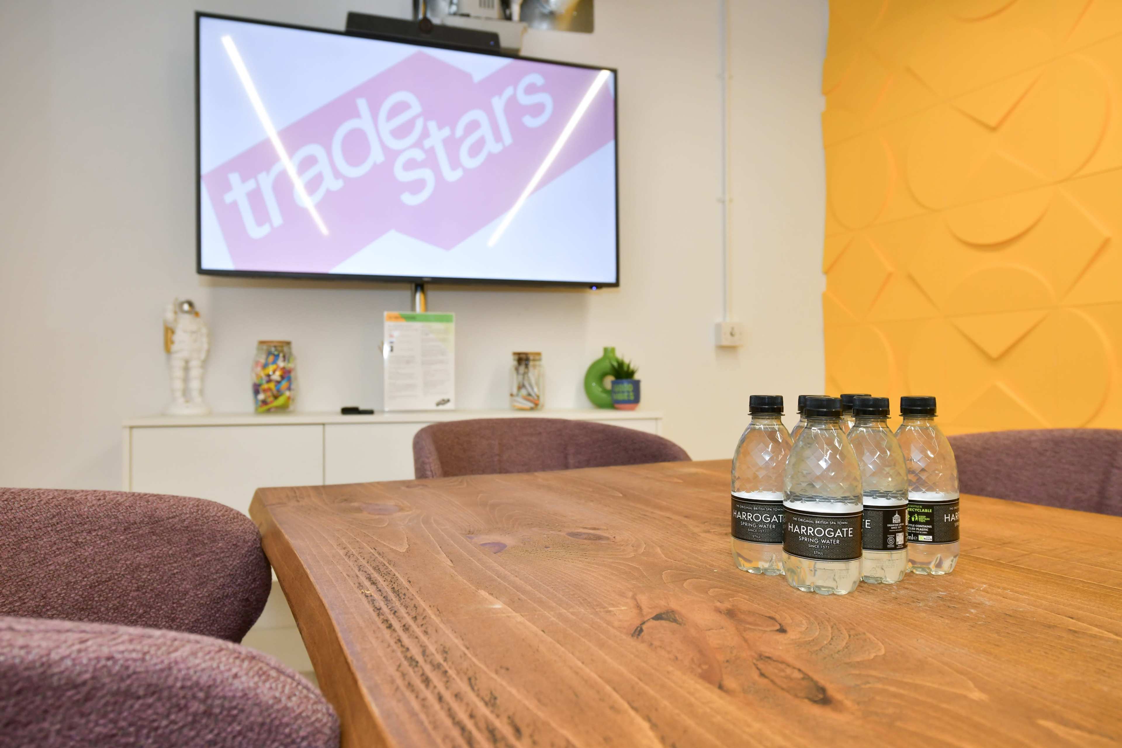 A conference room features a wooden table with labeled water bottles and a large screen displaying the "tradeStars" logo.