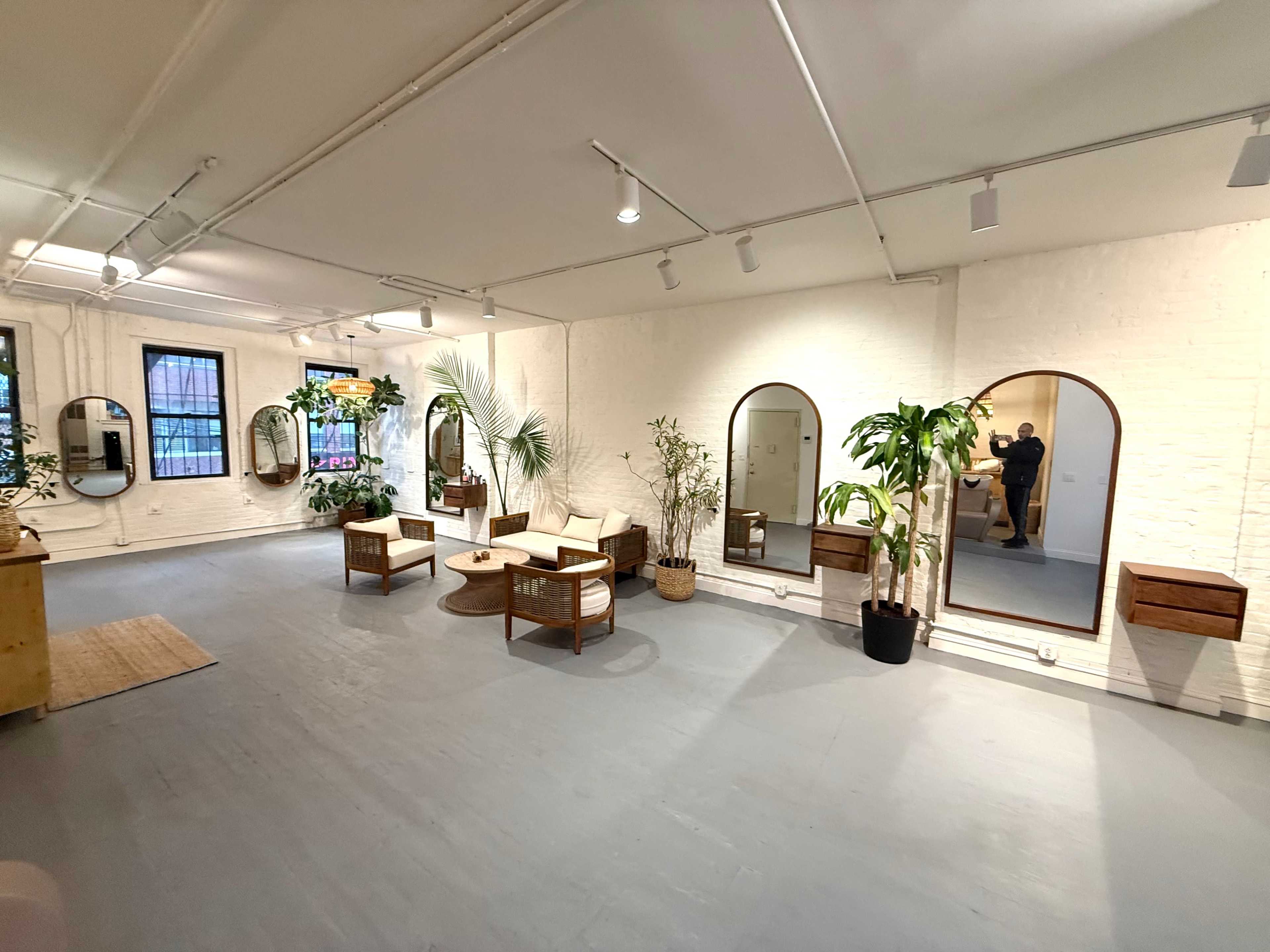 The image shows a spacious, well-lit interior with seating areas, decorative plants, and several mirrors mounted on the walls.