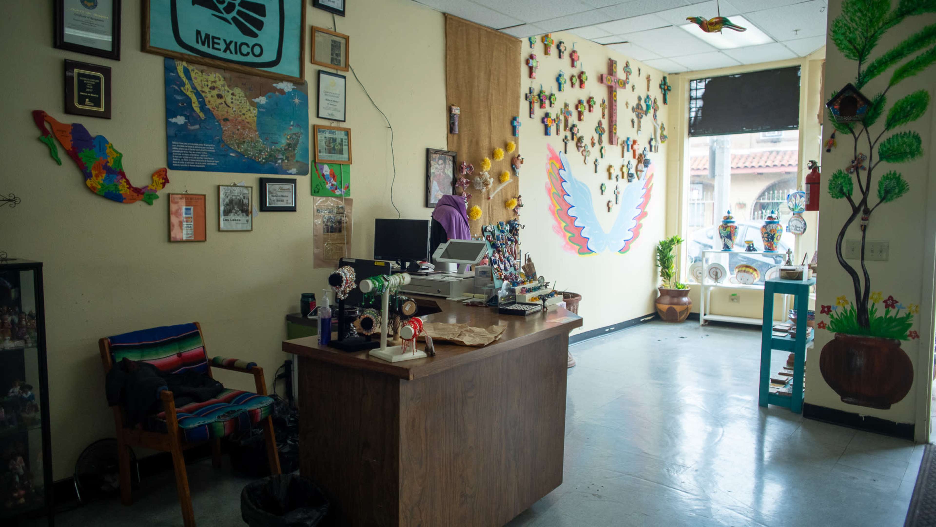 A colorful community center office decorated with maps of Mexico, artwork, and various handcrafted items for sale.