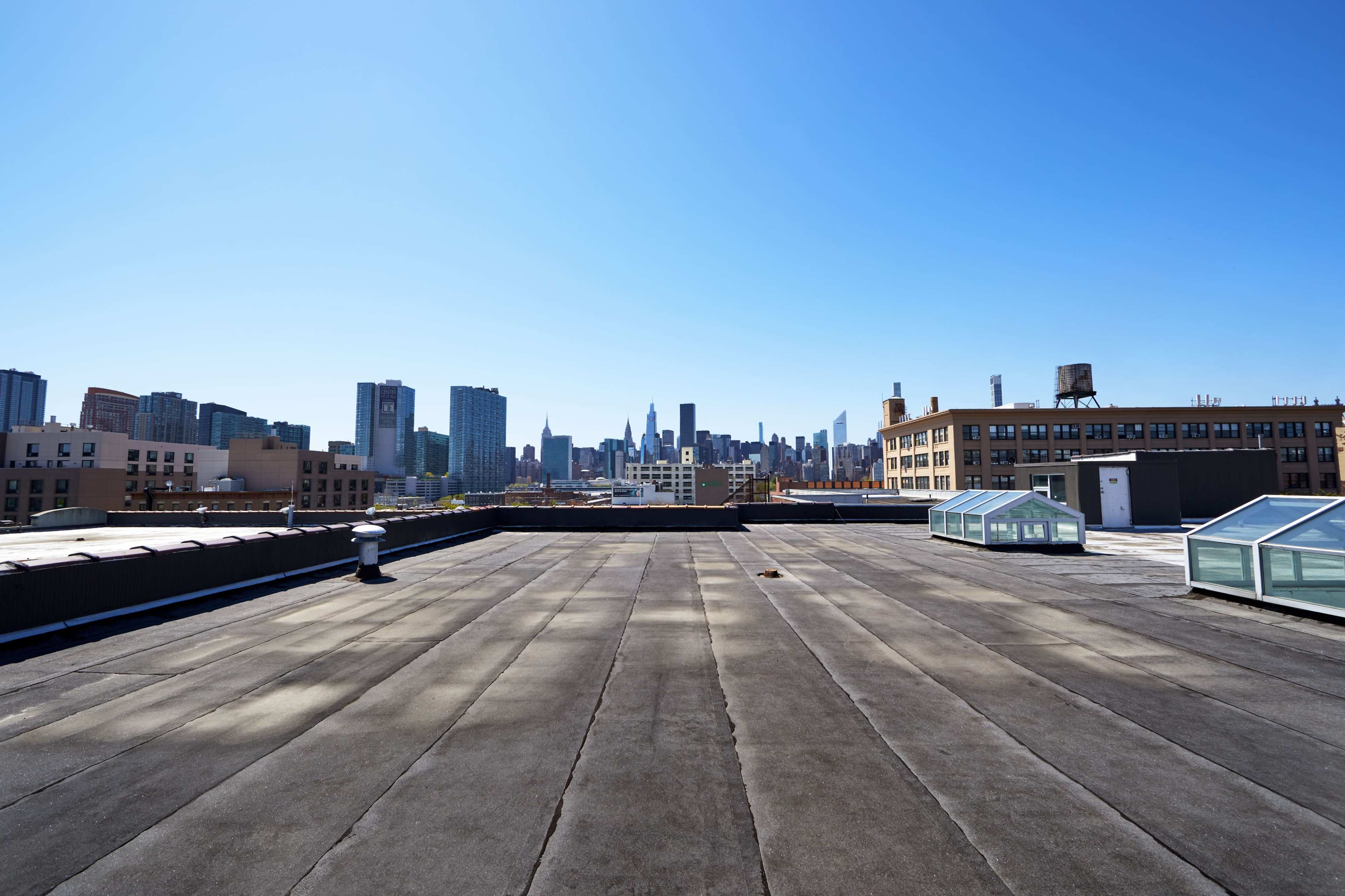 A flat rooftop offers a clear view of a skyline featuring tall buildings and a blue sky.