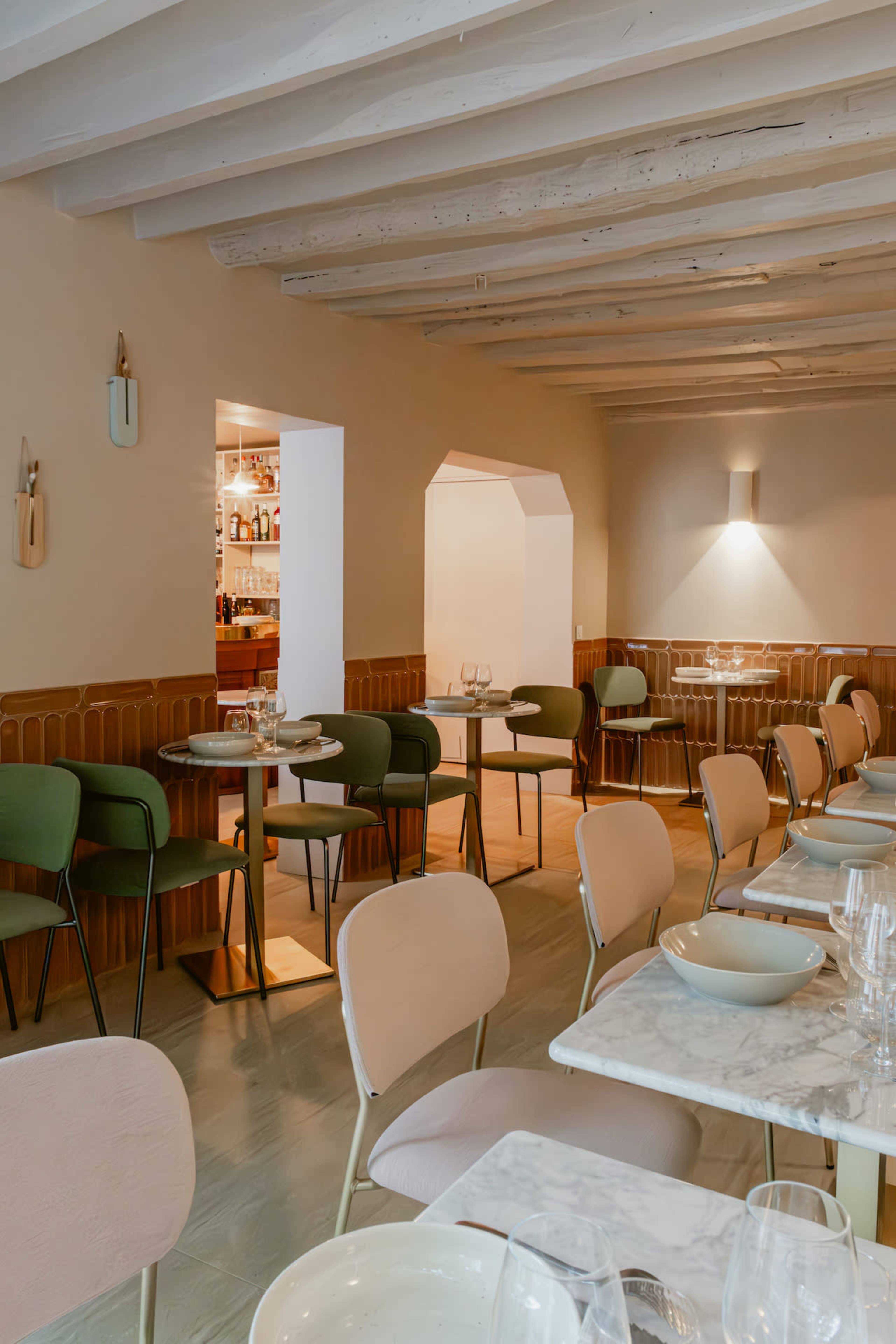 The image shows a modern restaurant interior with a combination of green and pink chairs, marble-topped tables, and warm lighting creating various seating arrangements.