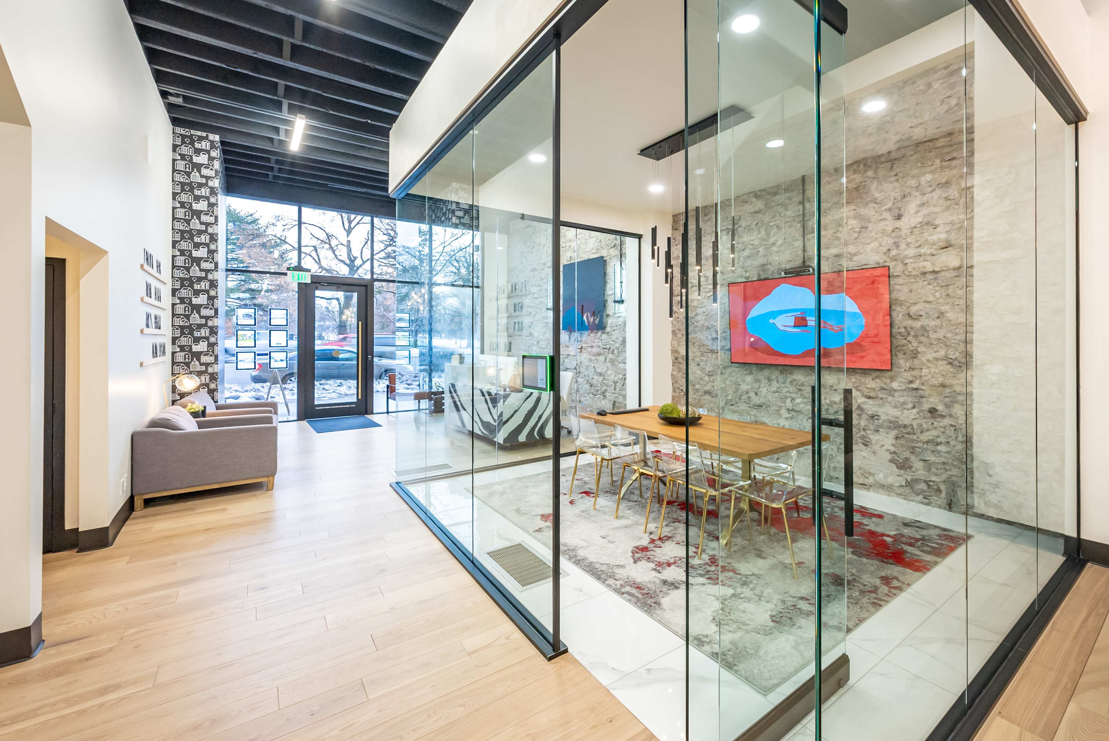 A modern office space features a glass meeting room with a wooden table and chairs, surrounded by a stylish living area and a large entrance.