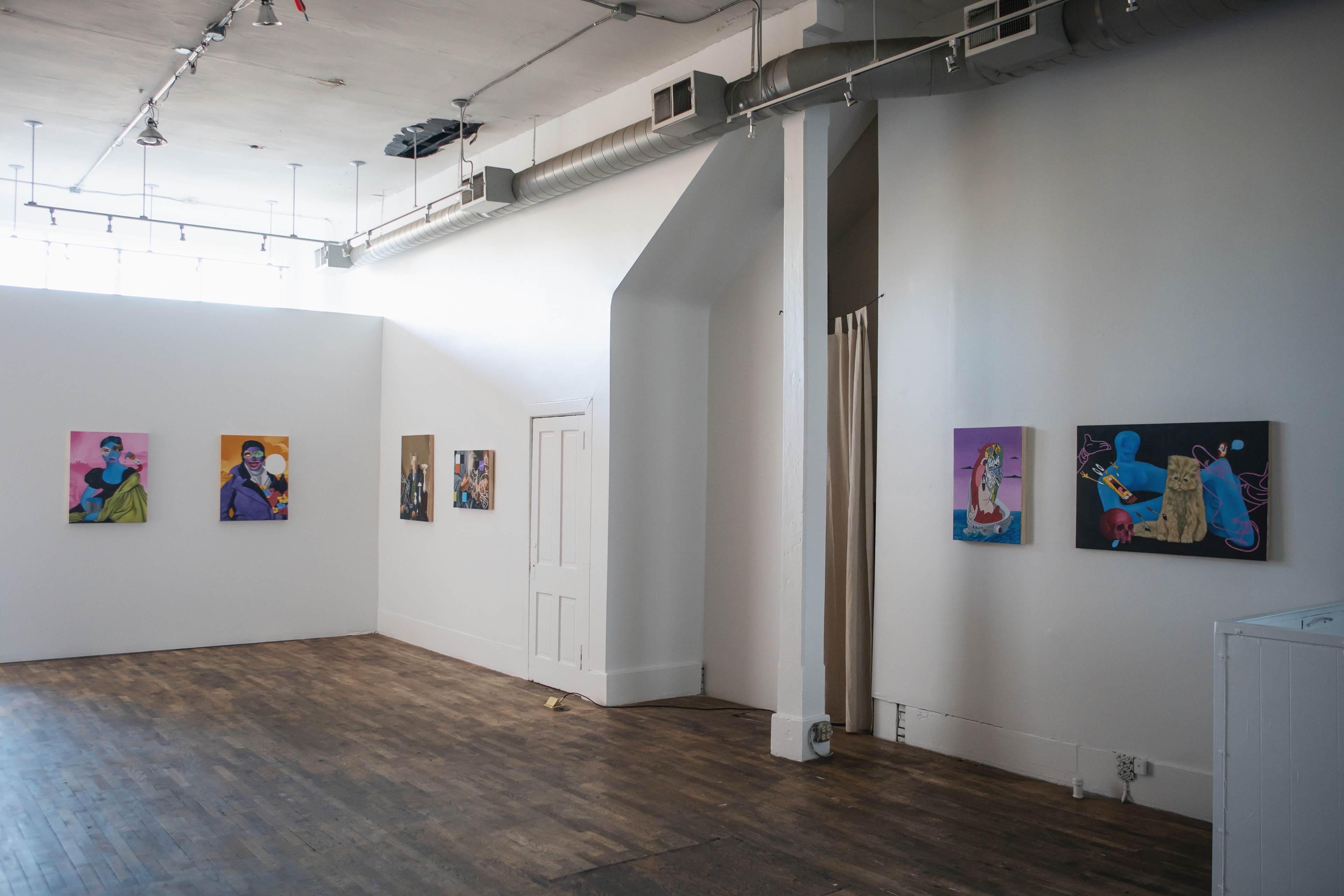 An art gallery with several colorful paintings displayed on white walls and wooden flooring.