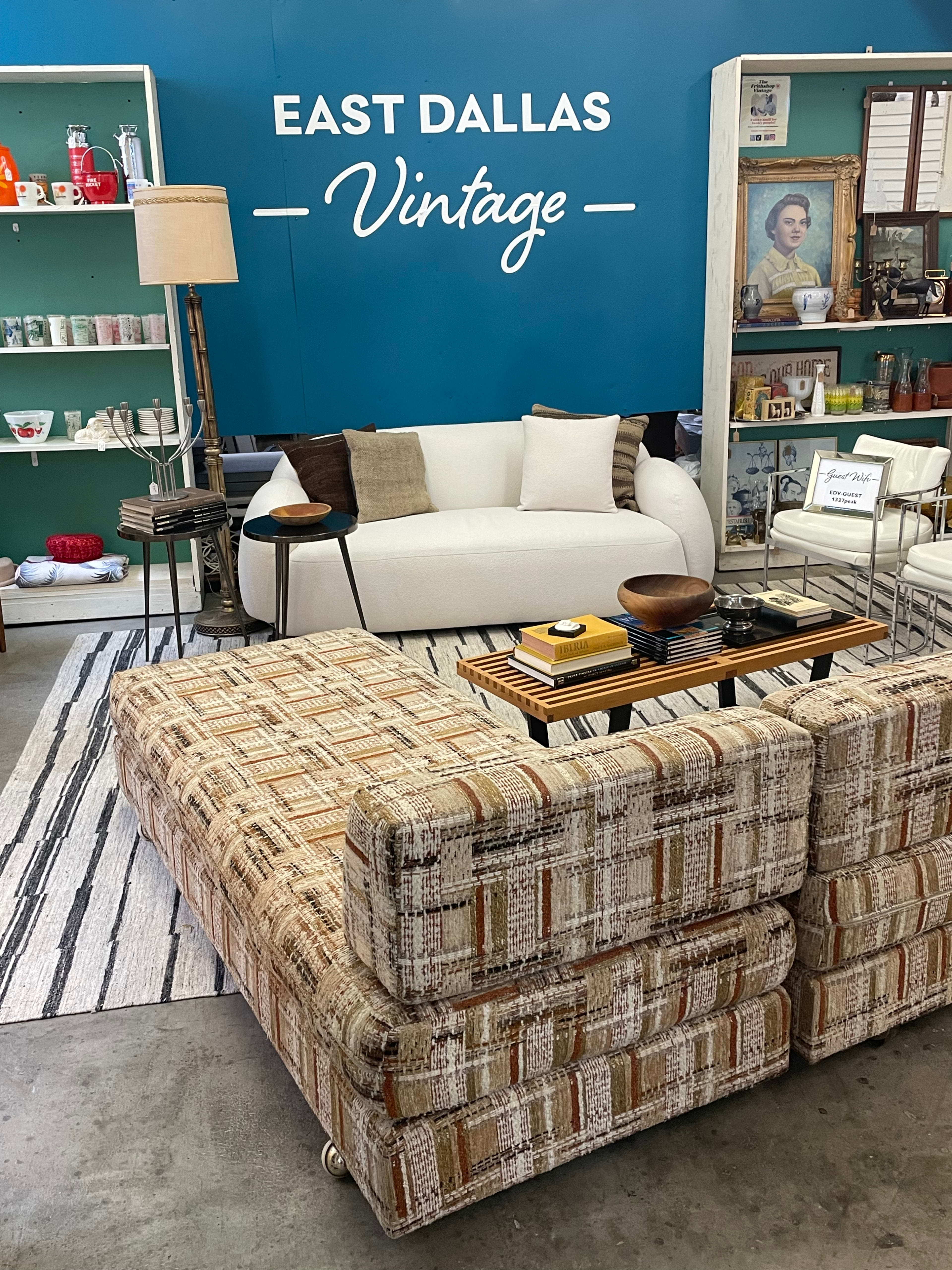 The image shows a vintage furniture display featuring a white couch, a patterned sectional sofa, and various decorative items against a teal wall with "EAST DALLAS Vintage" written on it.