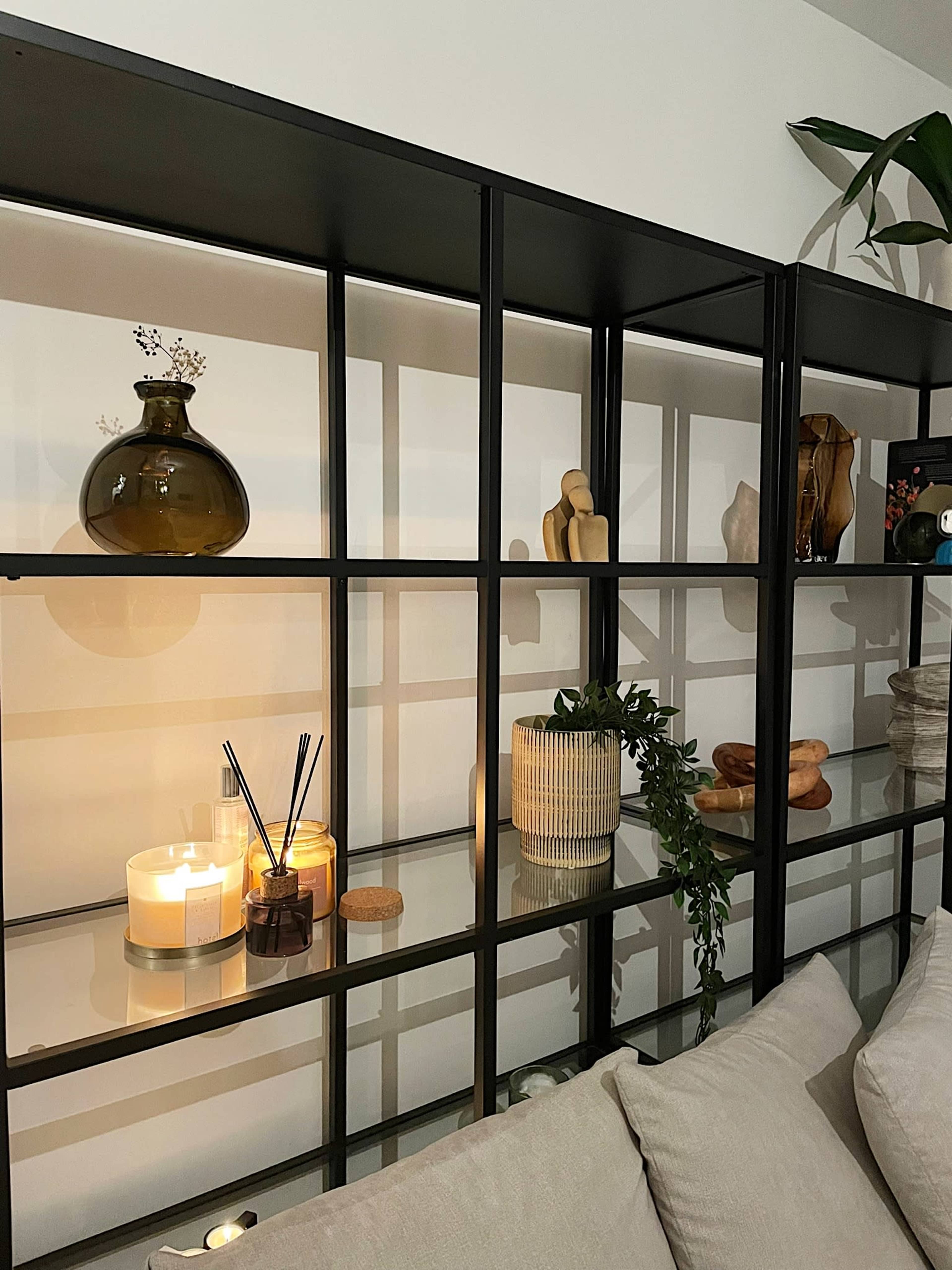 A modern shelving unit with decorative items, candles, and plants arranged on it, with a light source highlighting the display.