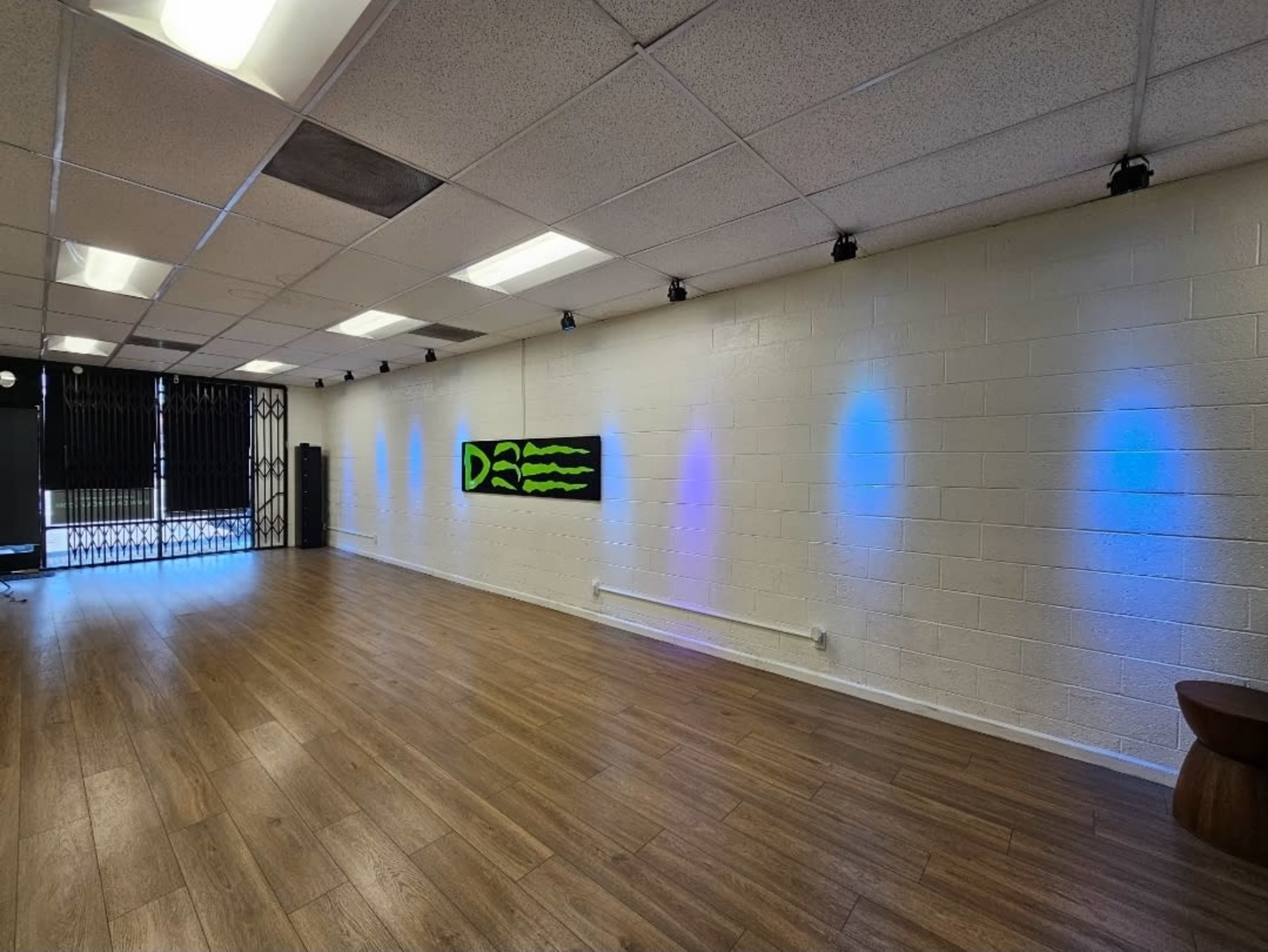 A spacious, well-lit interior room features wooden flooring, a mural with green and black graphics on a white wall, and blue lights illuminating the walls.