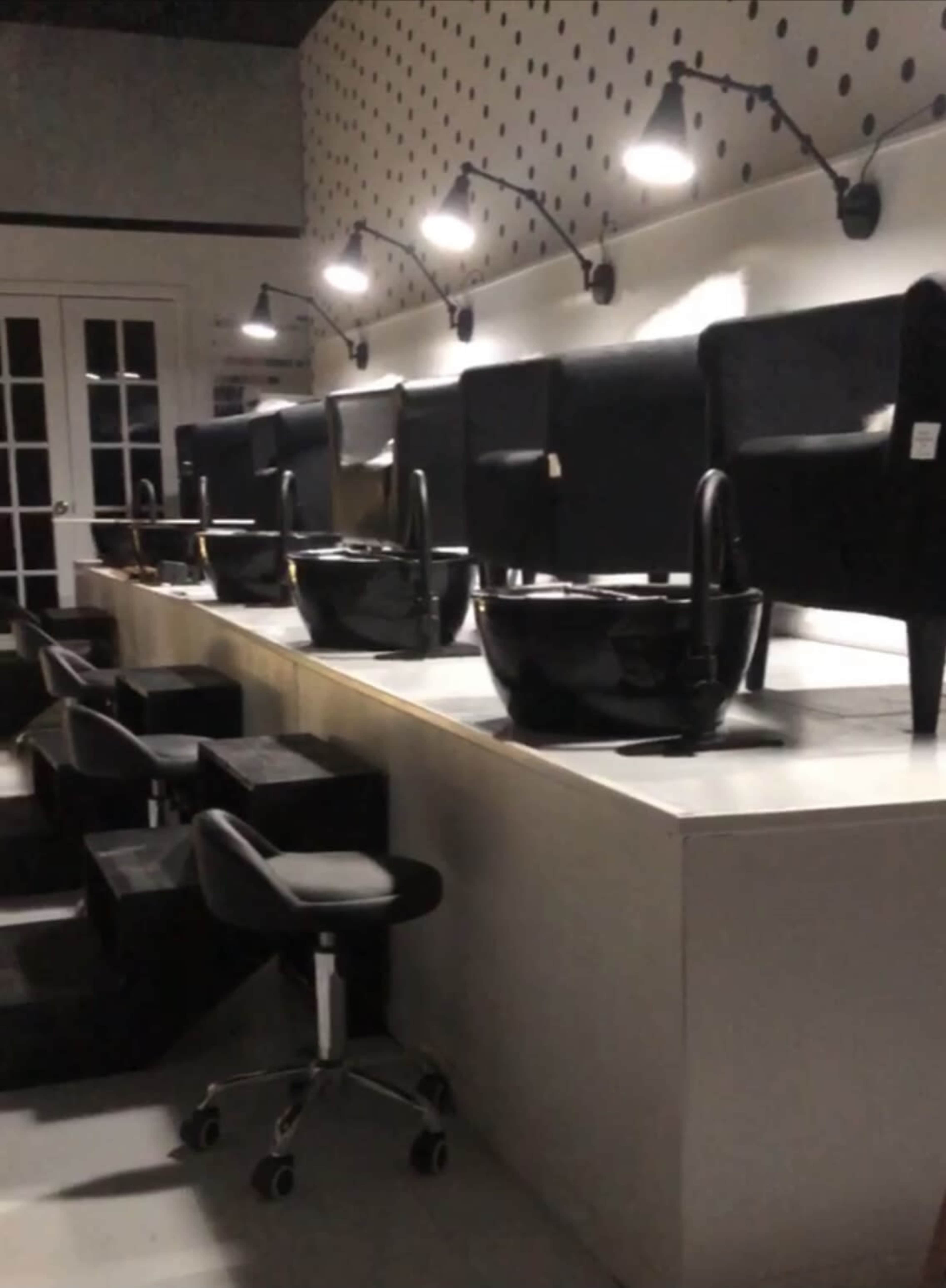 A manicure and pedicure station with multiple black chairs and bowls arranged along a light-colored countertop.