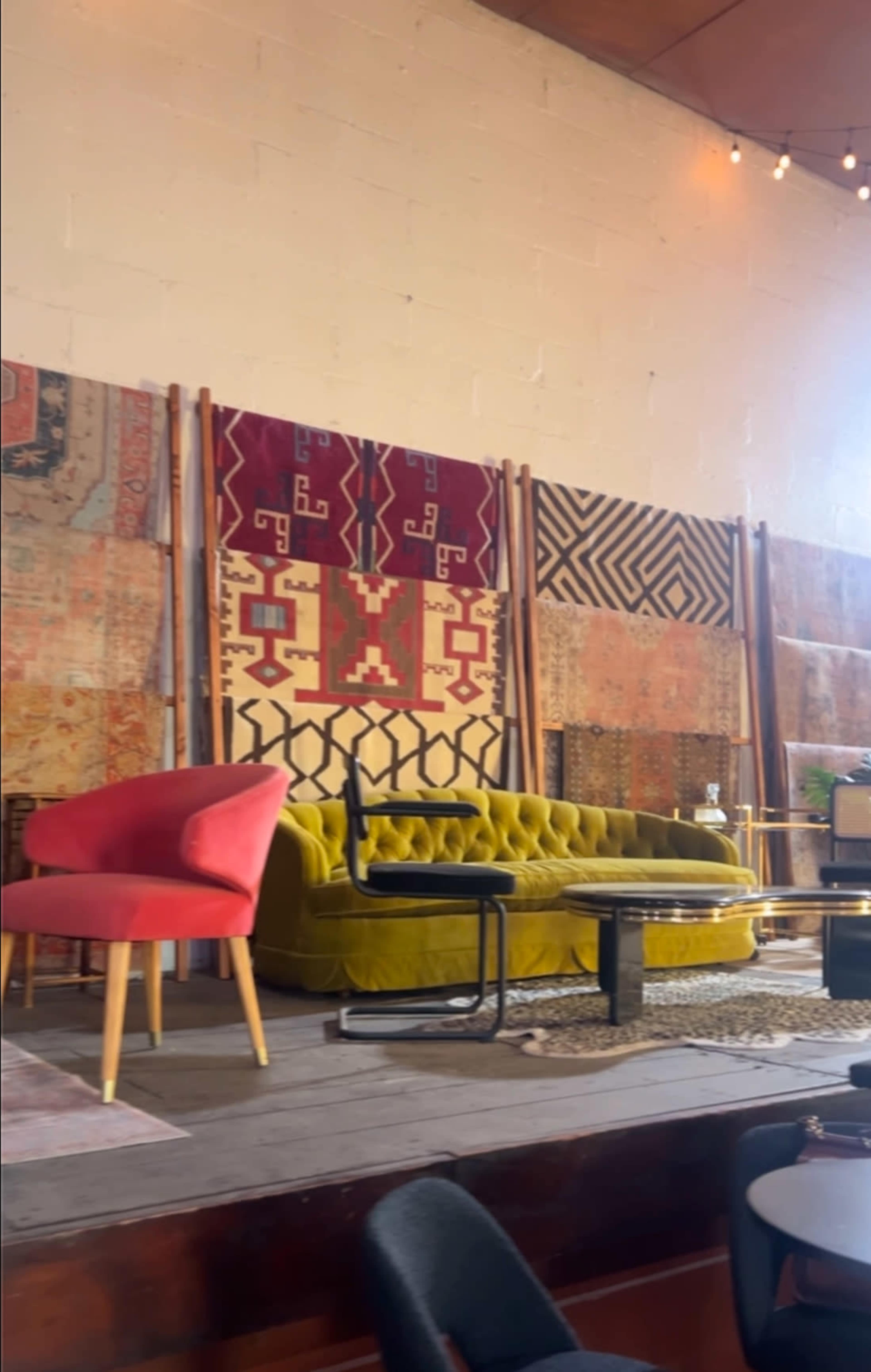 The scene shows a vibrant living space with a yellow velvet sofa, a pink chair, and patterned rugs displayed on the wall.