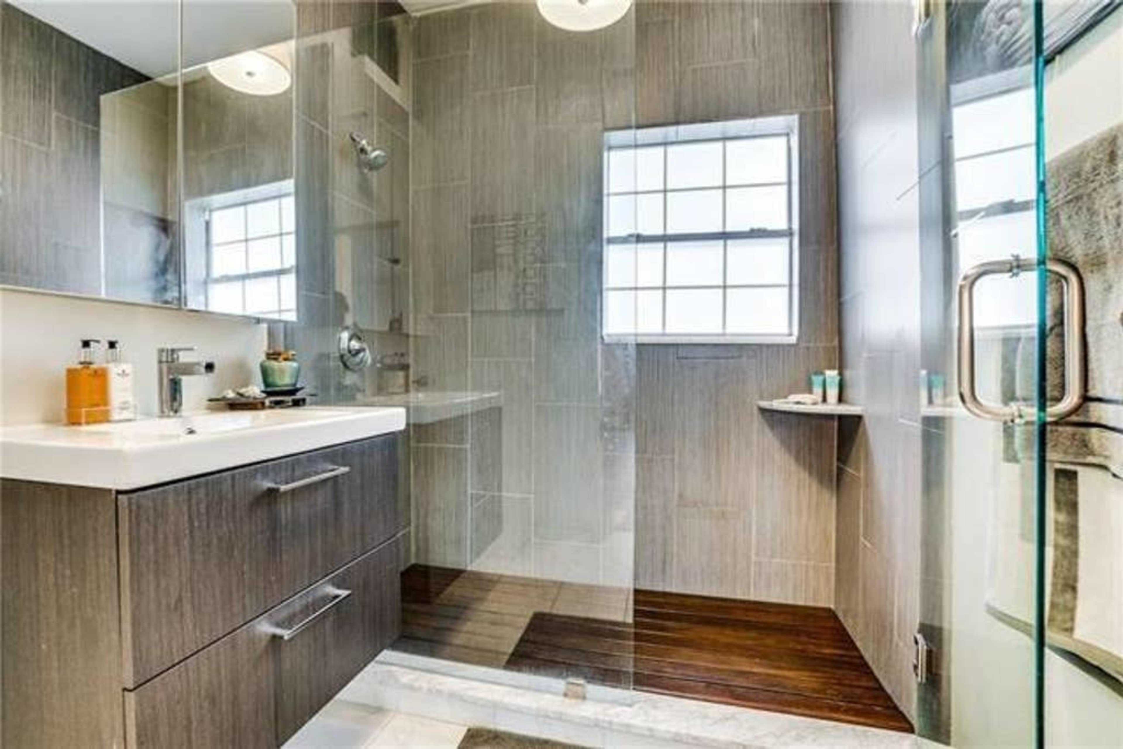 A modern bathroom featuring a glass shower, a sleek vanity with a sink, and a window allowing natural light.