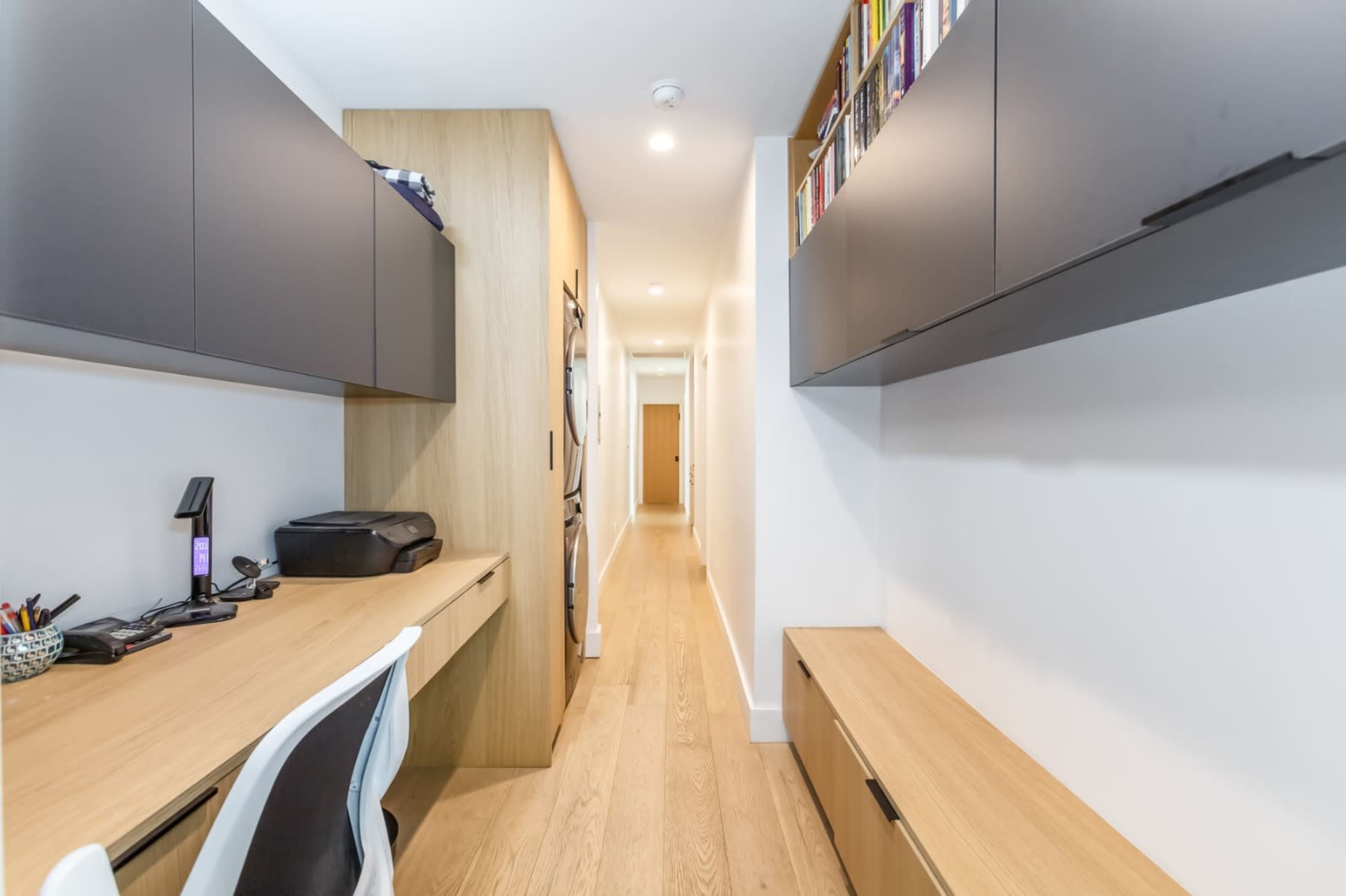 The image shows a narrow interior hallway with a desk and storage units along one side and a clear pathway leading to a door at the end.